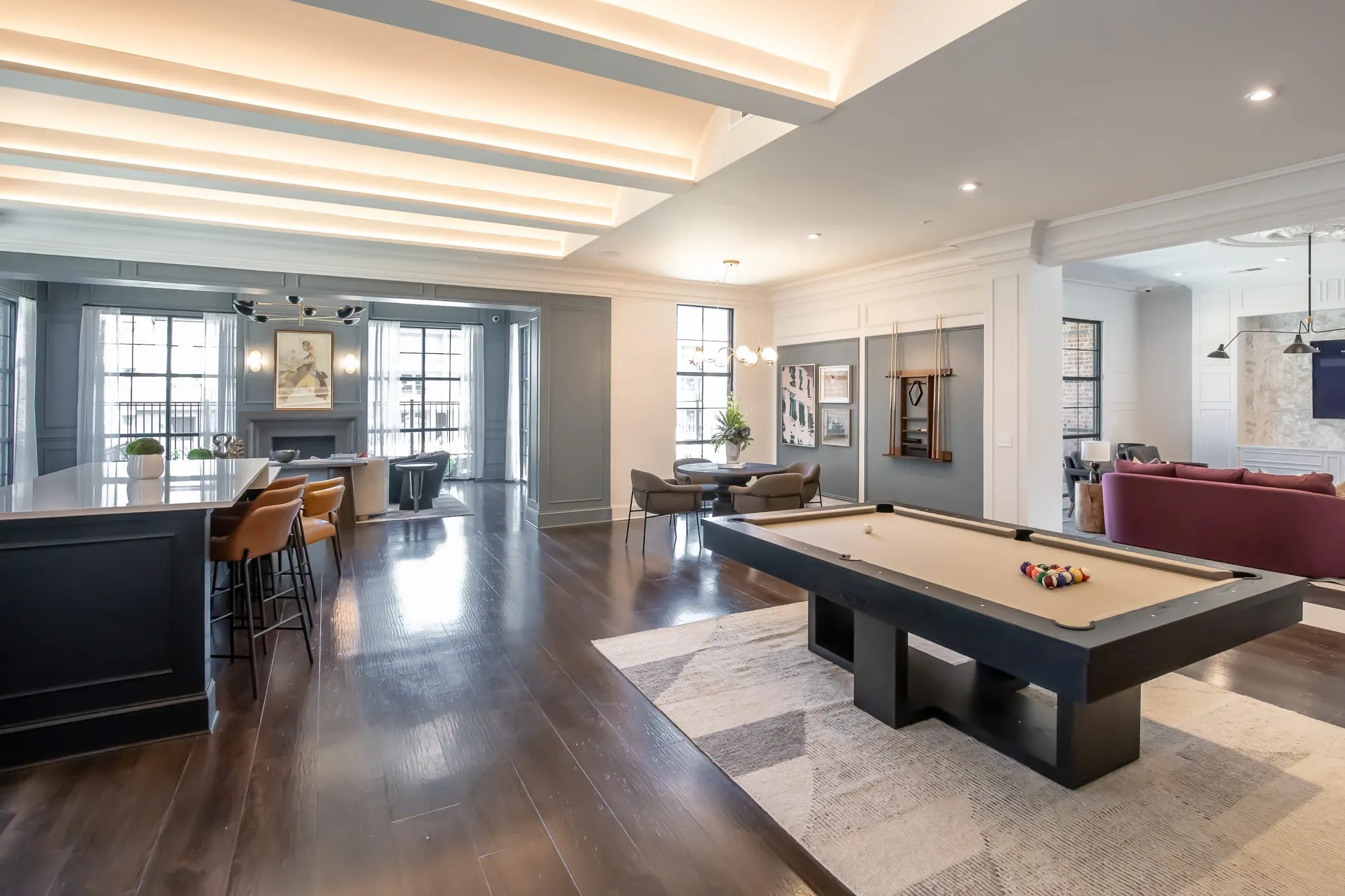 Multifamily amenity clubroom with a bar of orange leather stools beside the billiards table and a burgundy sofa beyond