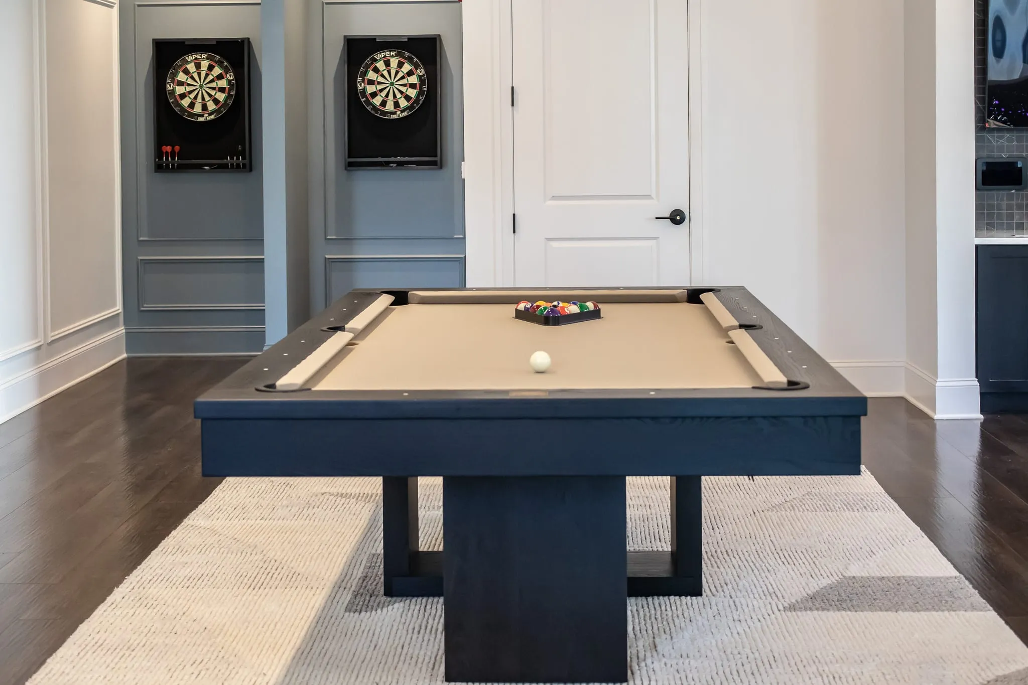 Multifamily amenity clubroom with two dartboard cabinets on a pale blue panelled wall beside the billiards table