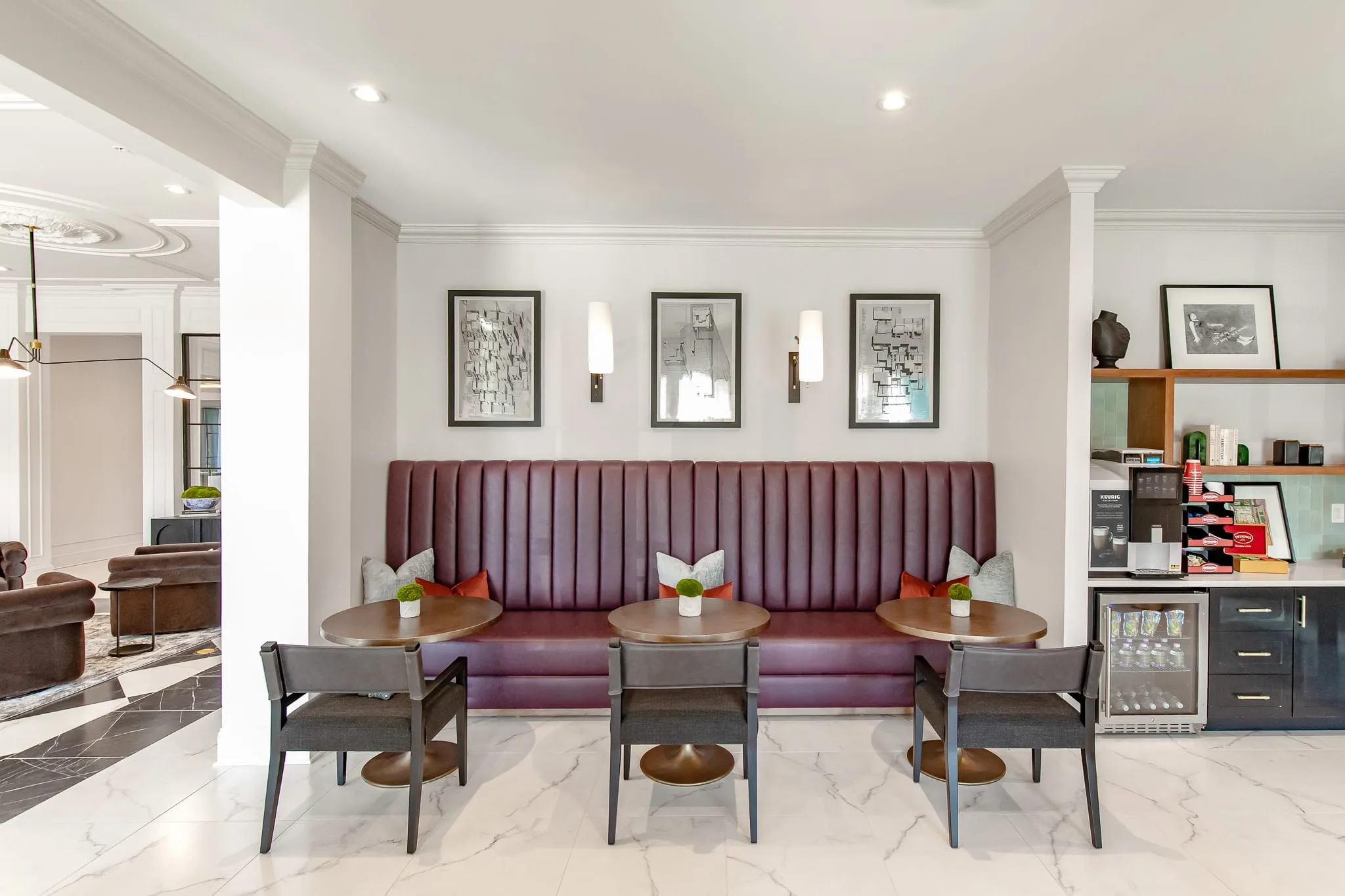 Multifamily amenity coffee lounge with a burgundy channel tufted banquette and cafe tables on marble by the beverage station