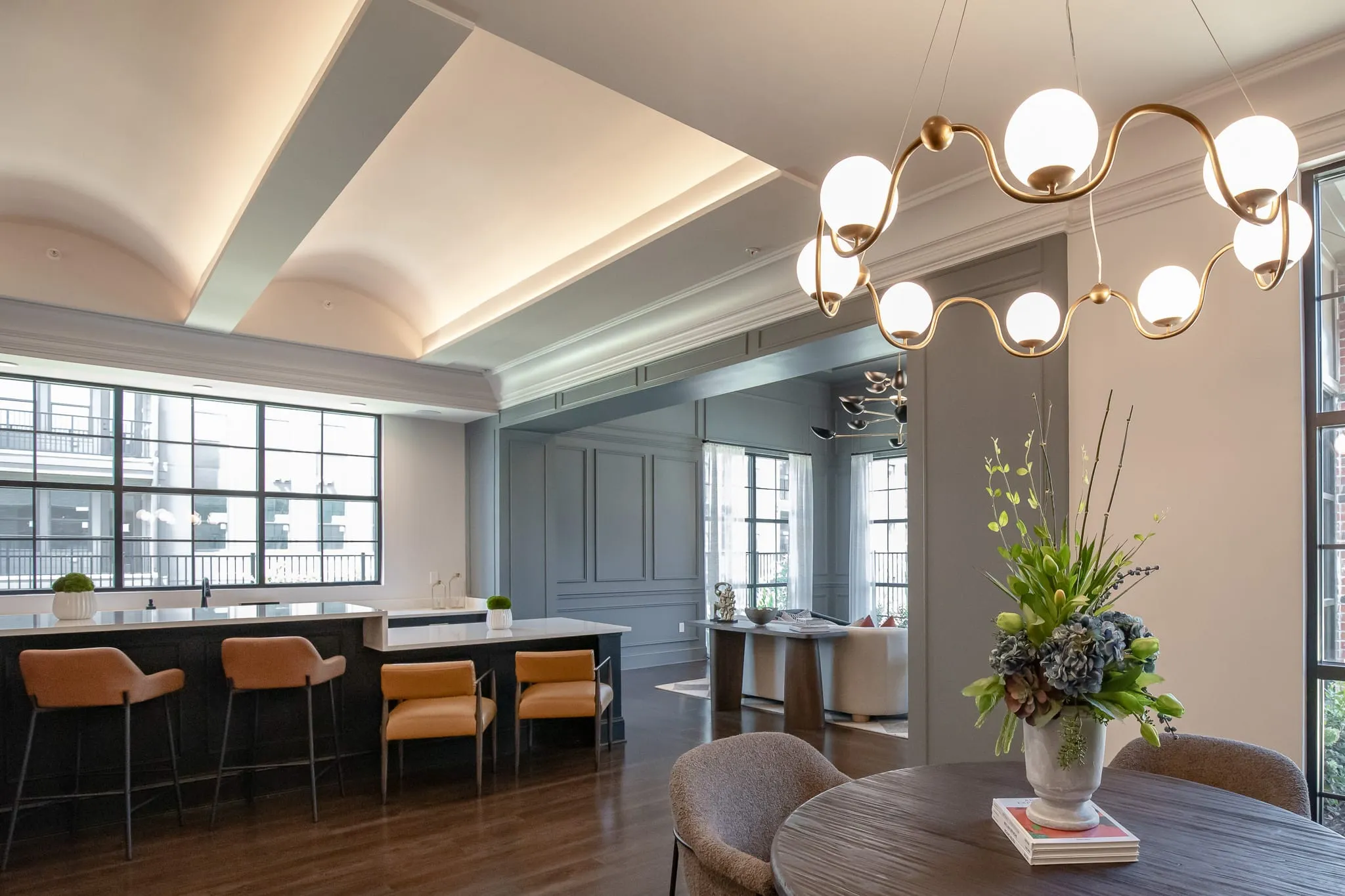 Multifamily amenity clubroom, orange leather stools at the kitchen counter under vaulted coves, a brass globe chandelier