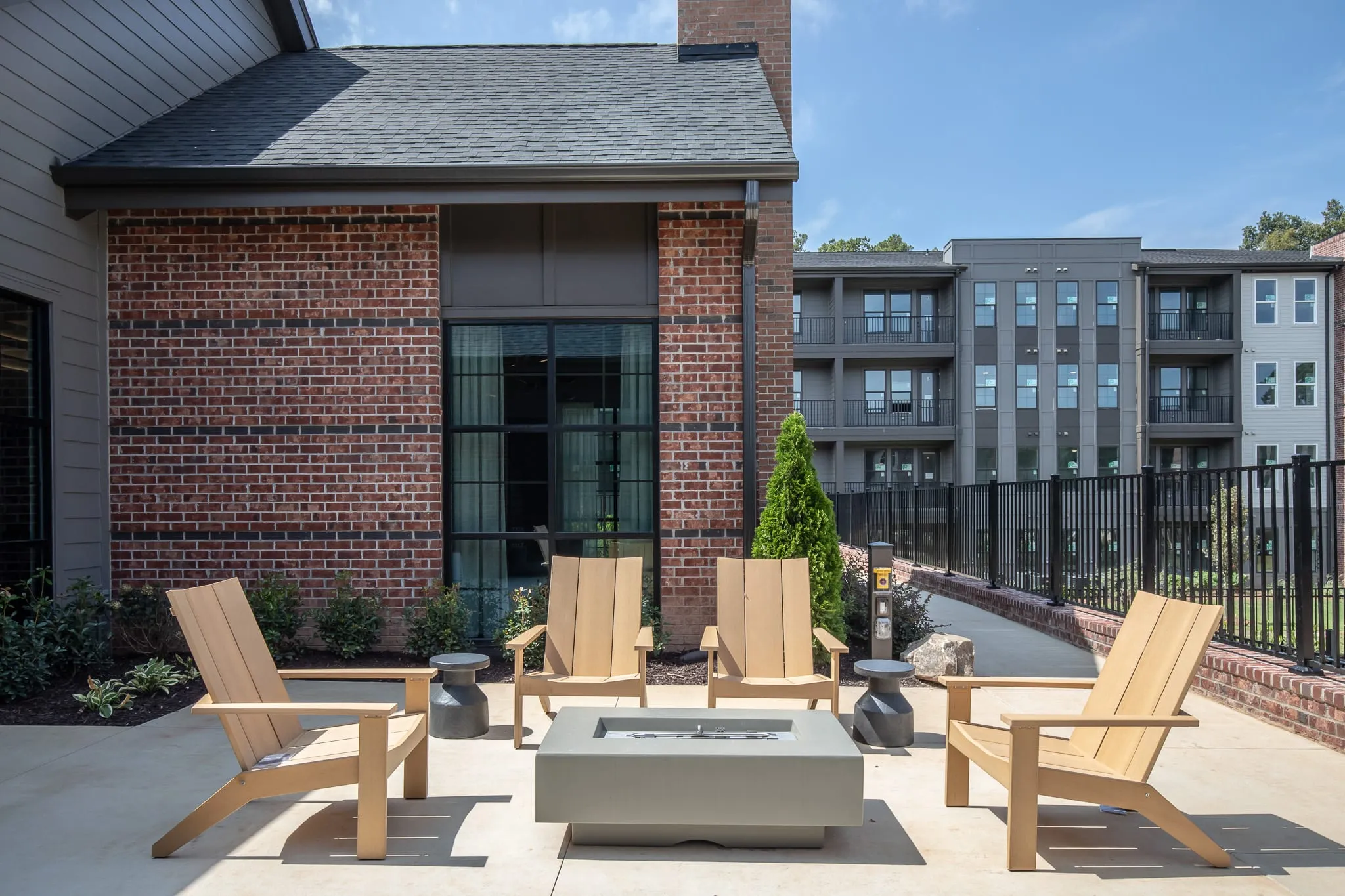 Multifamily community firepit terrace with wood Adirondack chairs around a concrete gas firepit beside the brick clubhouse