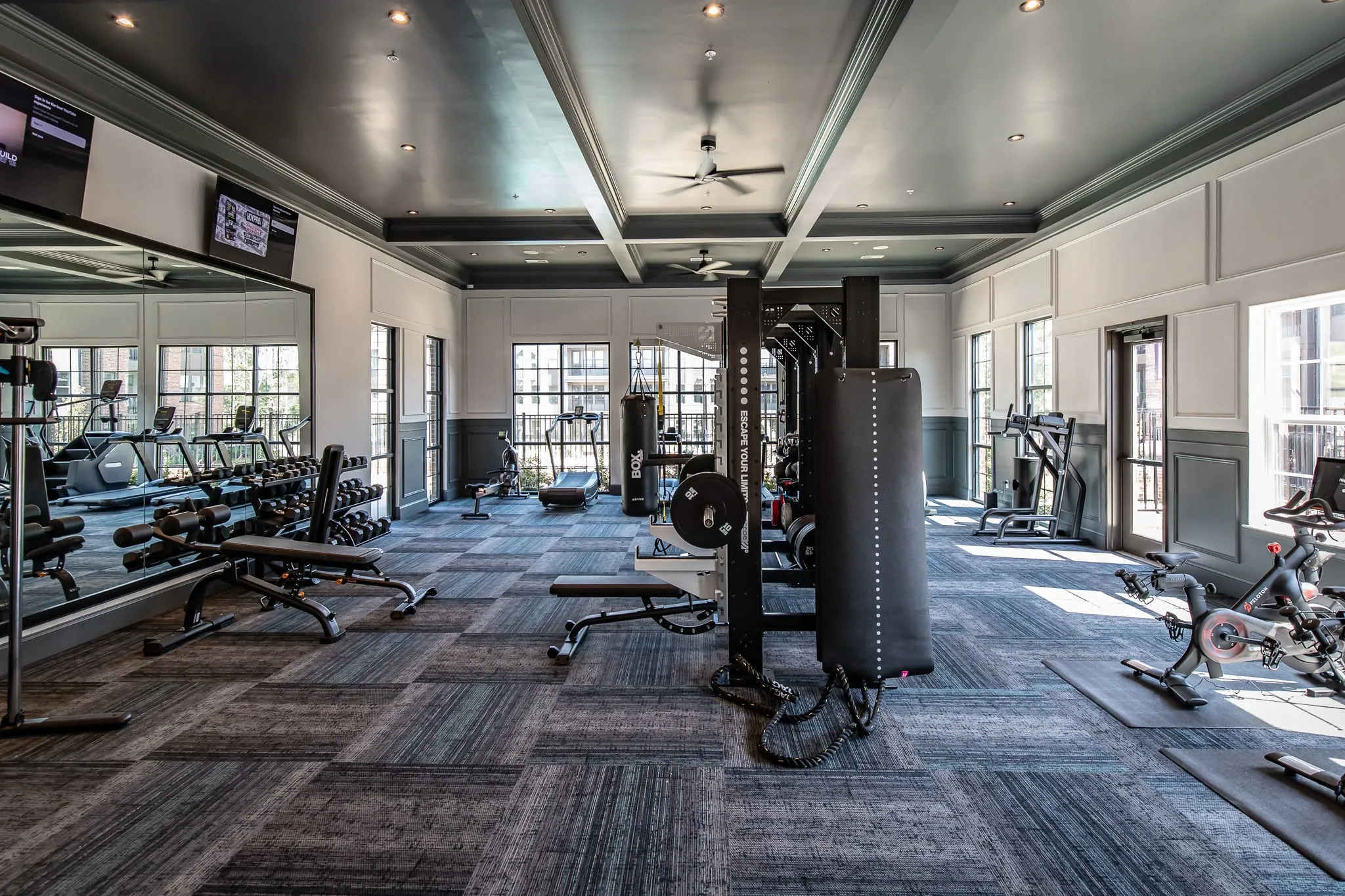 Multifamily amenity fitness center with cardio machines and free weights under a dark coffered ceiling, a mirrored wall