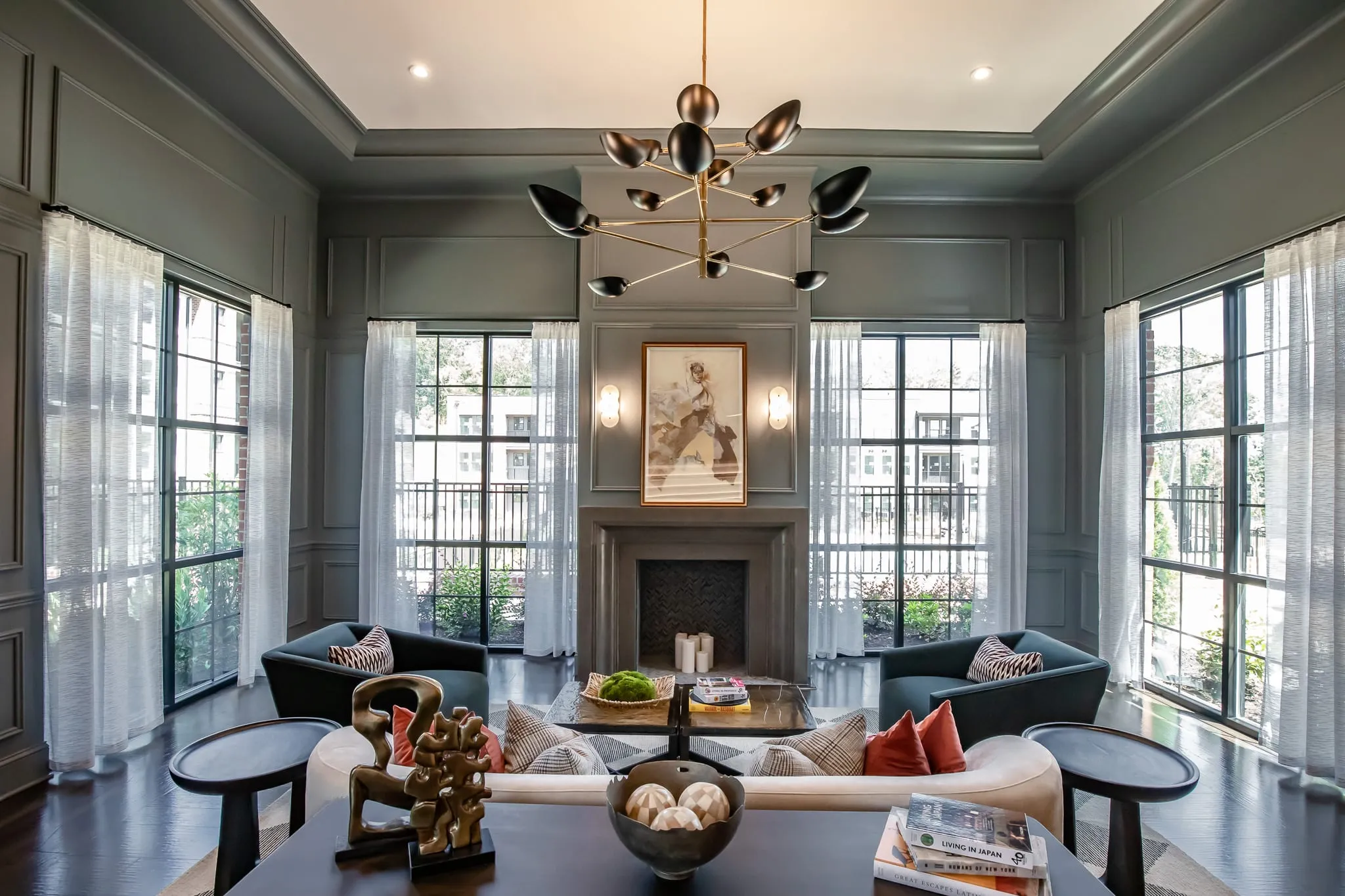 Multifamily amenity great room with a marble fireplace between tall windows under a brass sputnik chandelier, sage panelling