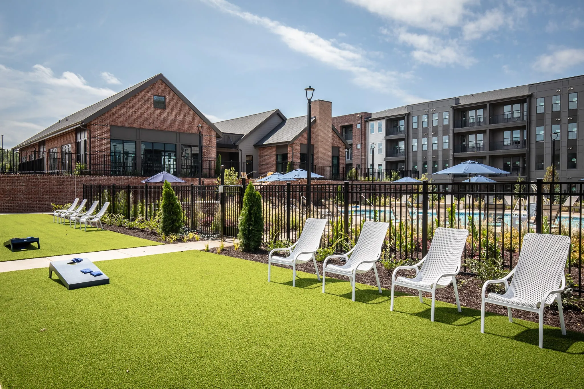 Multifamily community lawn with cornhole boards on turf beside white loungers, the pool beyond