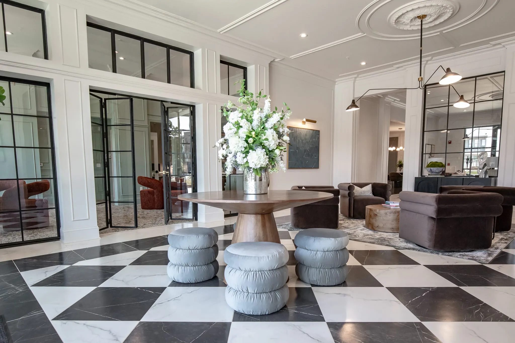 Multifamily amenity lobby on checkerboard marble with a round table of white flowers, puff stools and brown velvet chairs
