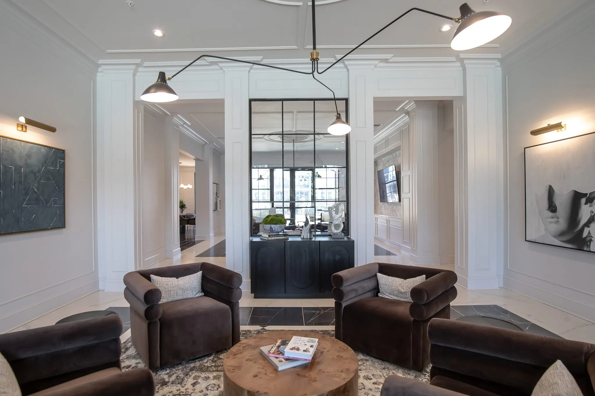 Multifamily amenity lobby lounge with brown velvet club chairs around a burl table under a black multi-arm light
