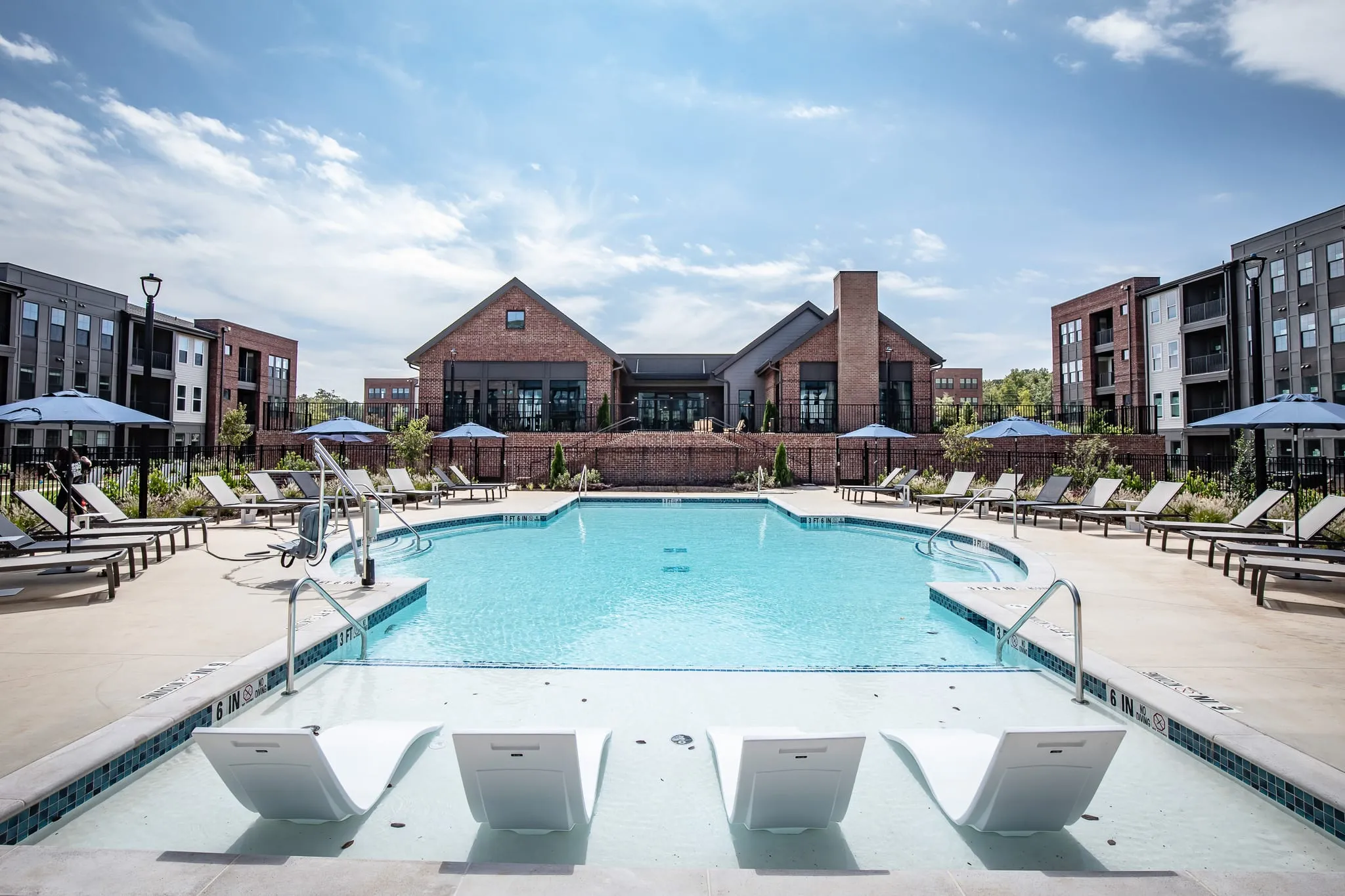 Multifamily community pool terrace with loungers and umbrellas along the water in front of the brick clubhouse