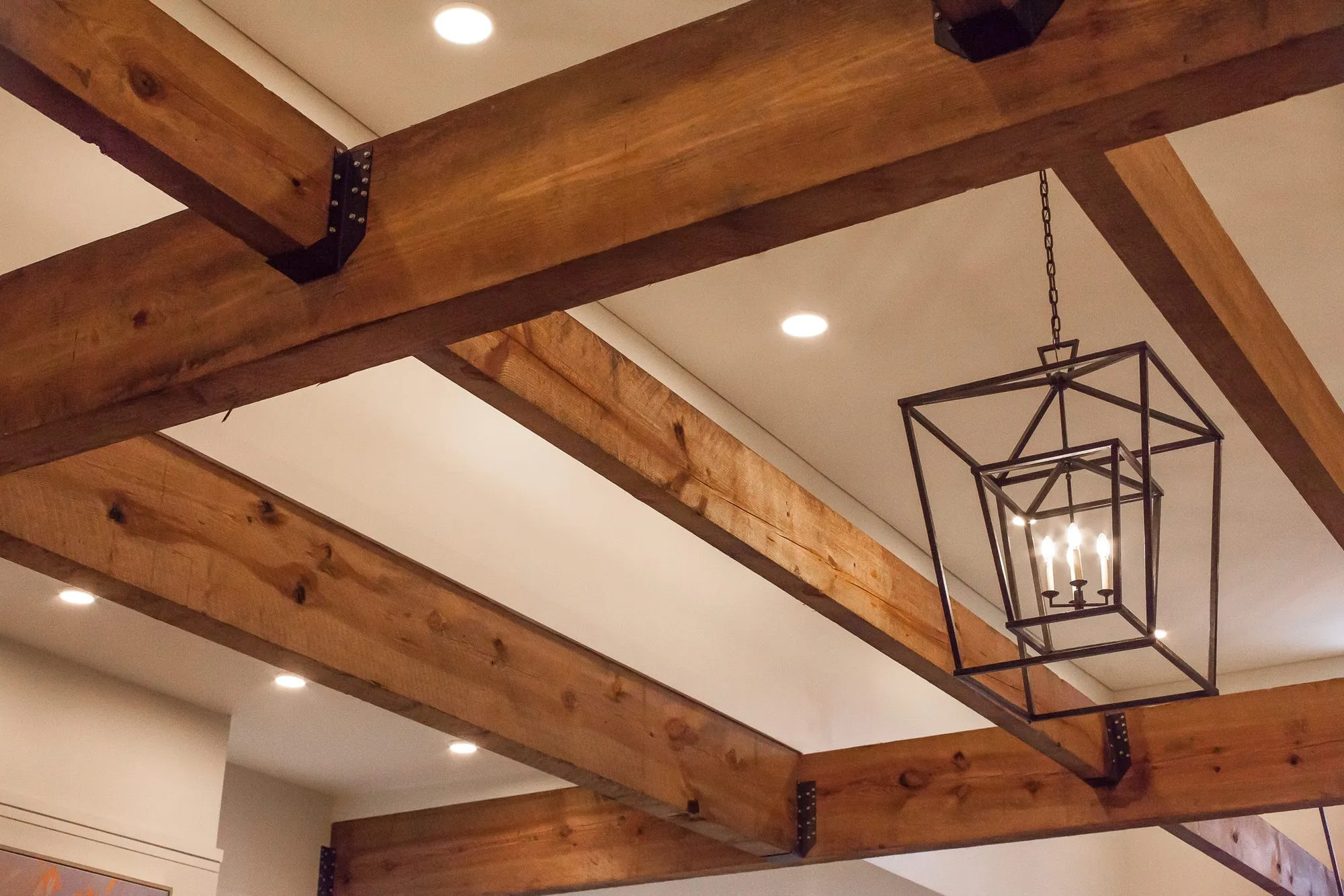 Senior living interior detail: rough timber ceiling beams with black iron brackets around a black cage lantern pendant