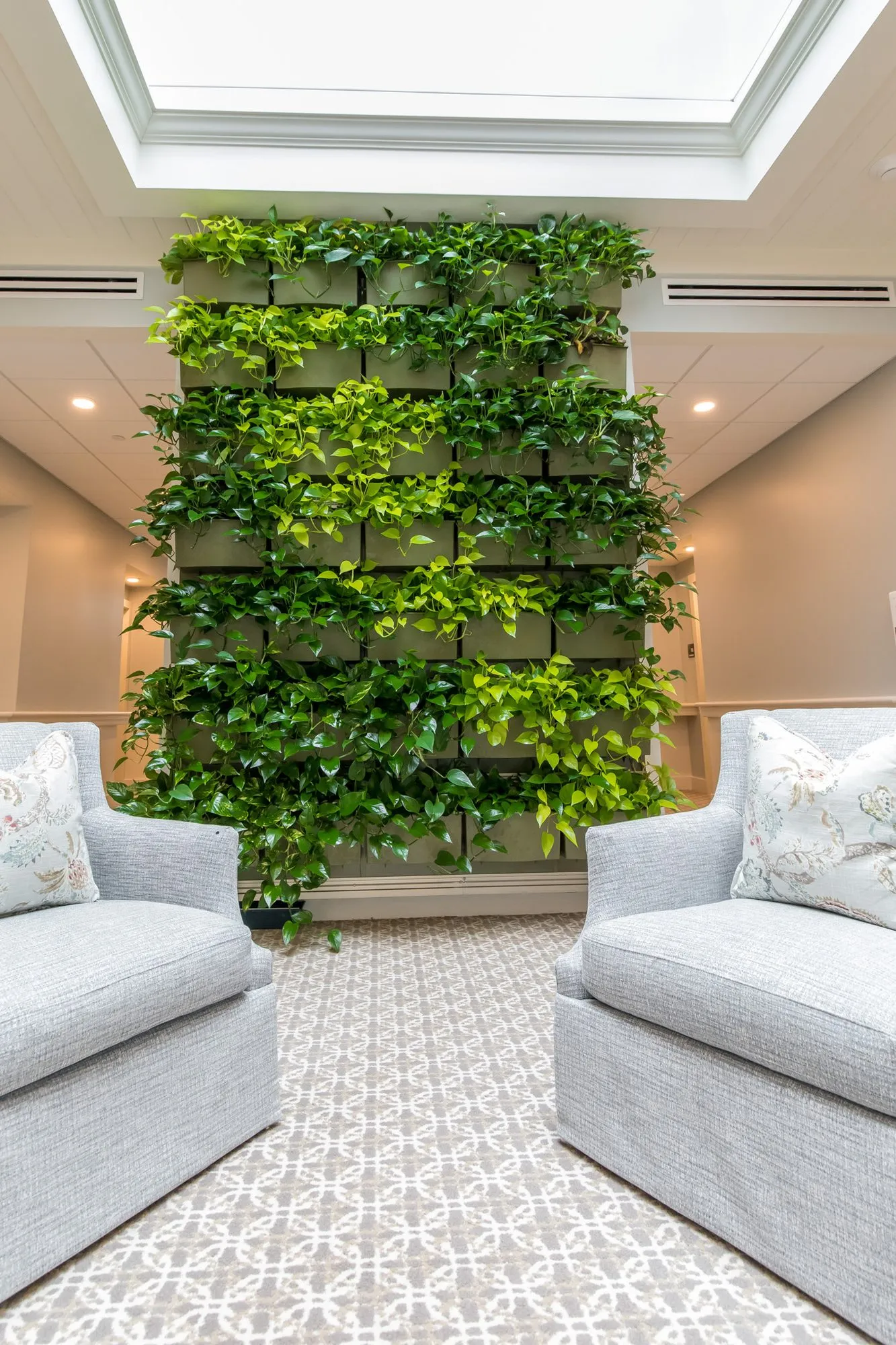 Senior living lounge with a full-height living wall of green planters rising toward a skylight between two pale armchairs