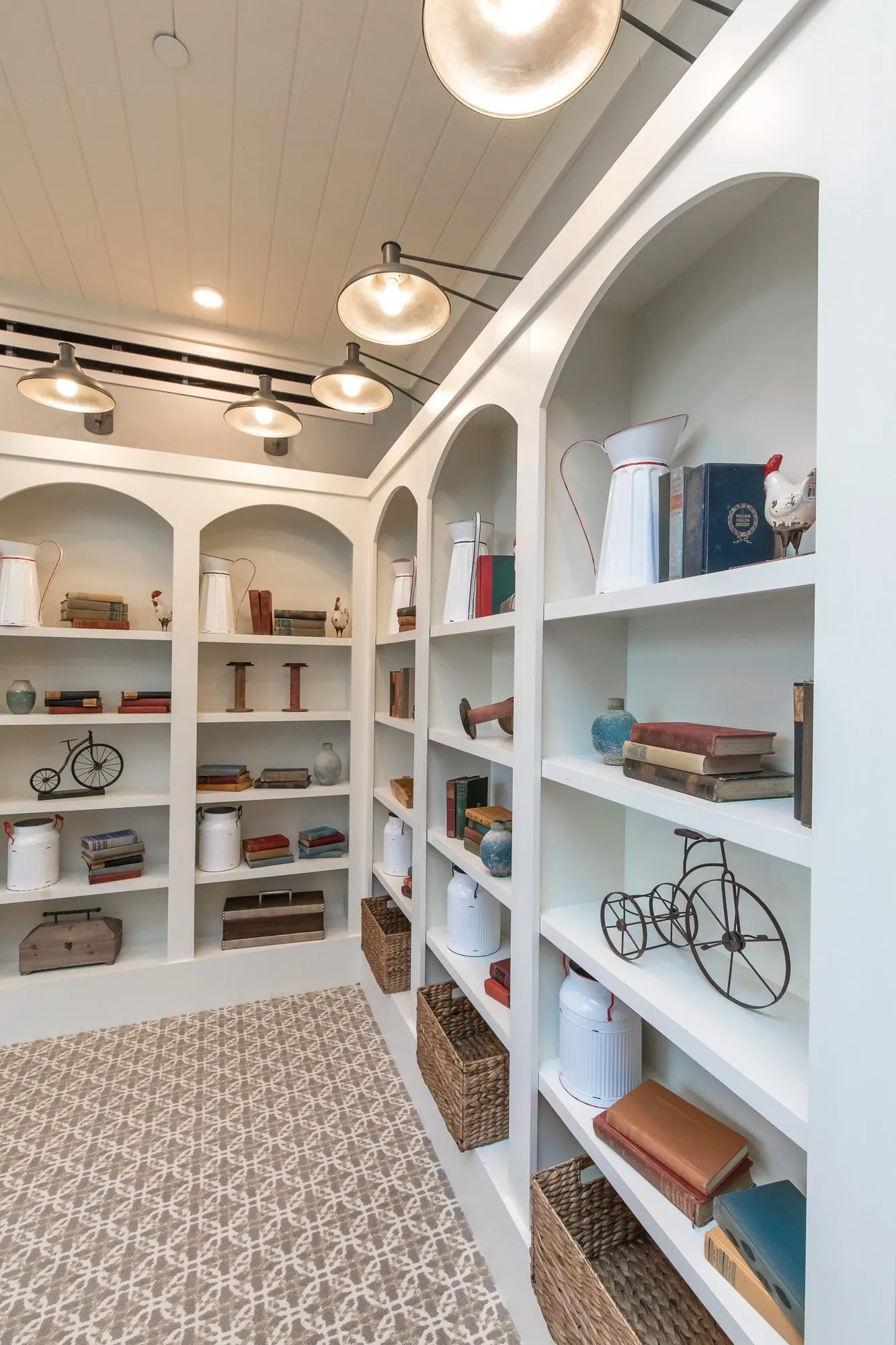 Senior living interior detail: arched white bookcases styled with old books, white pitchers and a toy penny-farthing