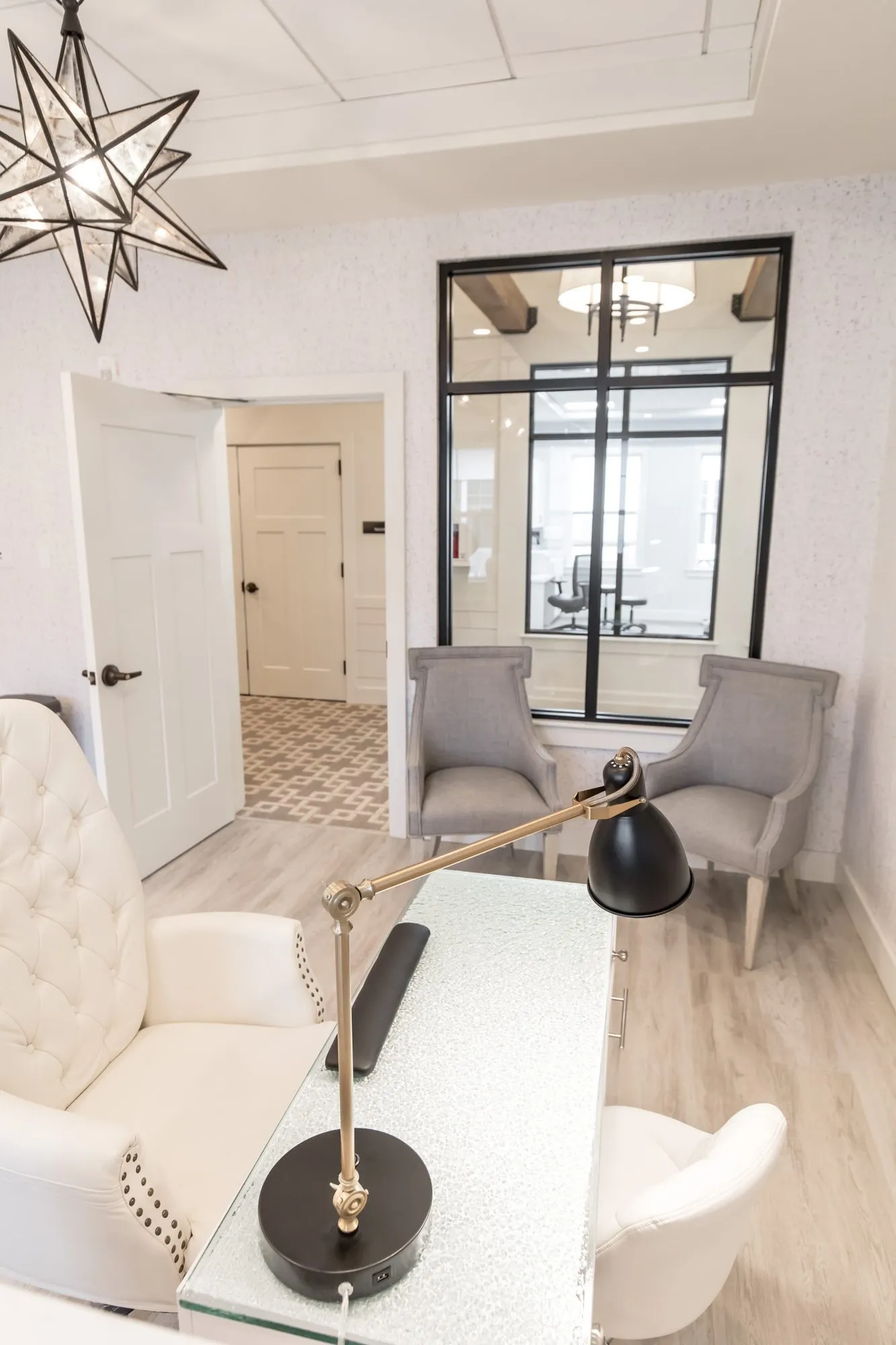 Senior living office with a white tufted armchair at a glass desk with a black task lamp under a star pendant