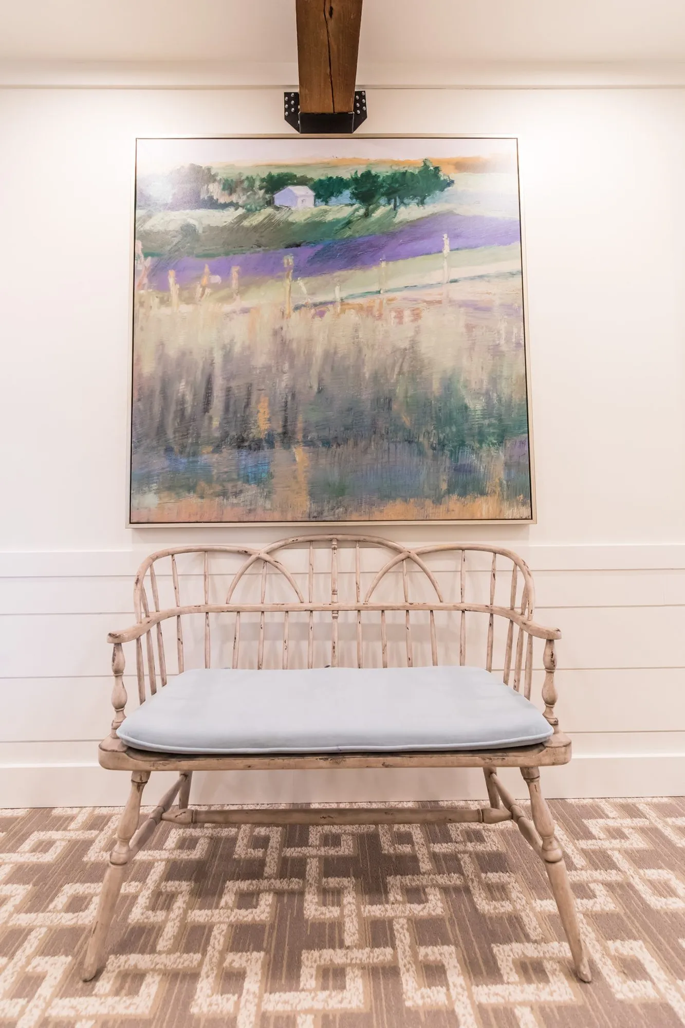 Senior living interior detail: bentwood settee with a pale blue cushion below an abstract landscape painting on shiplap