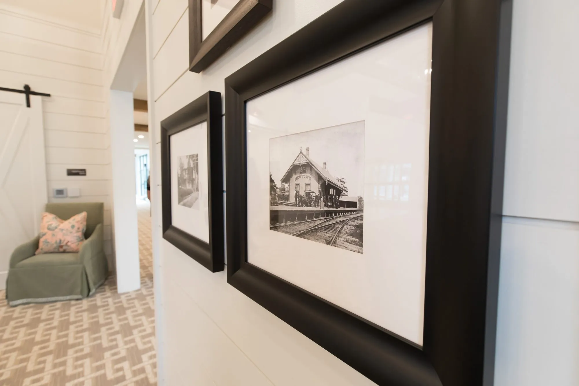 Senior living interior detail: framed black and white photograph of a railway depot on shiplap, a sage armchair beyond