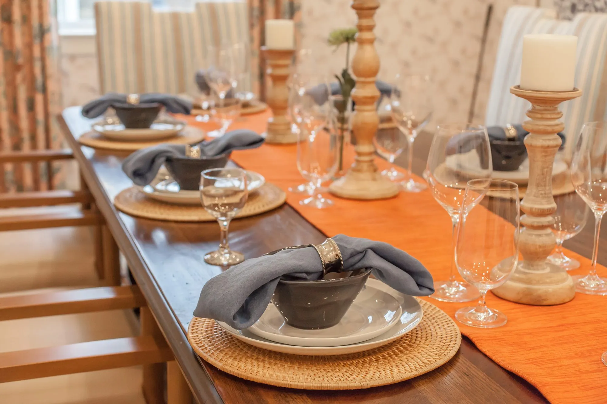 Senior living interior detail: dining table set with grey napkins in stoneware bowls, rattan chargers and an orange runner