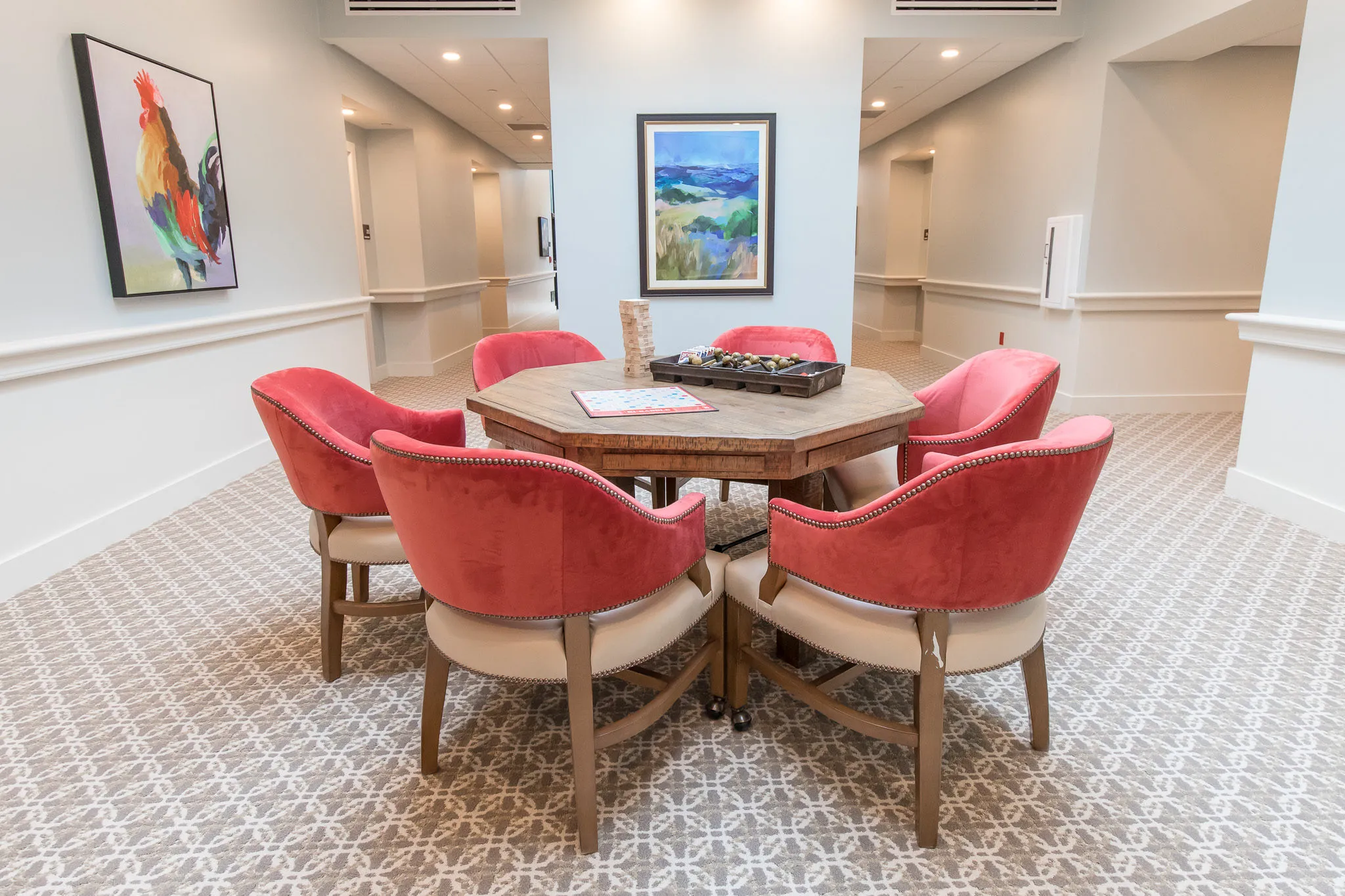 Senior living card room with six coral velvet chairs on casters around an octagonal games table
