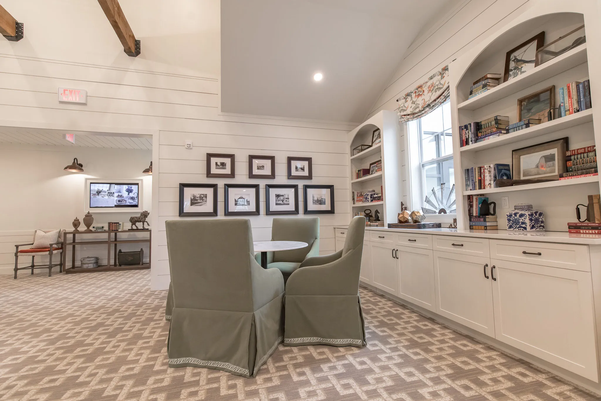 Senior living den with arched bookcases and framed prints above sage skirted chairs at a bistro table
