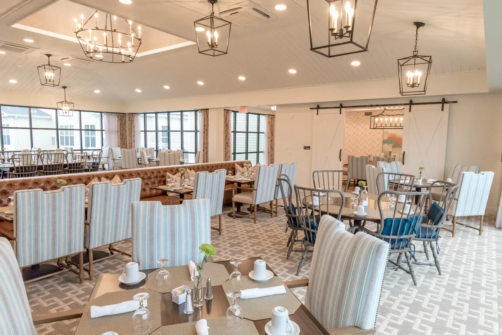 Senior living dining room with striped slipcovered chairs and spindle-back seats below black lantern pendants