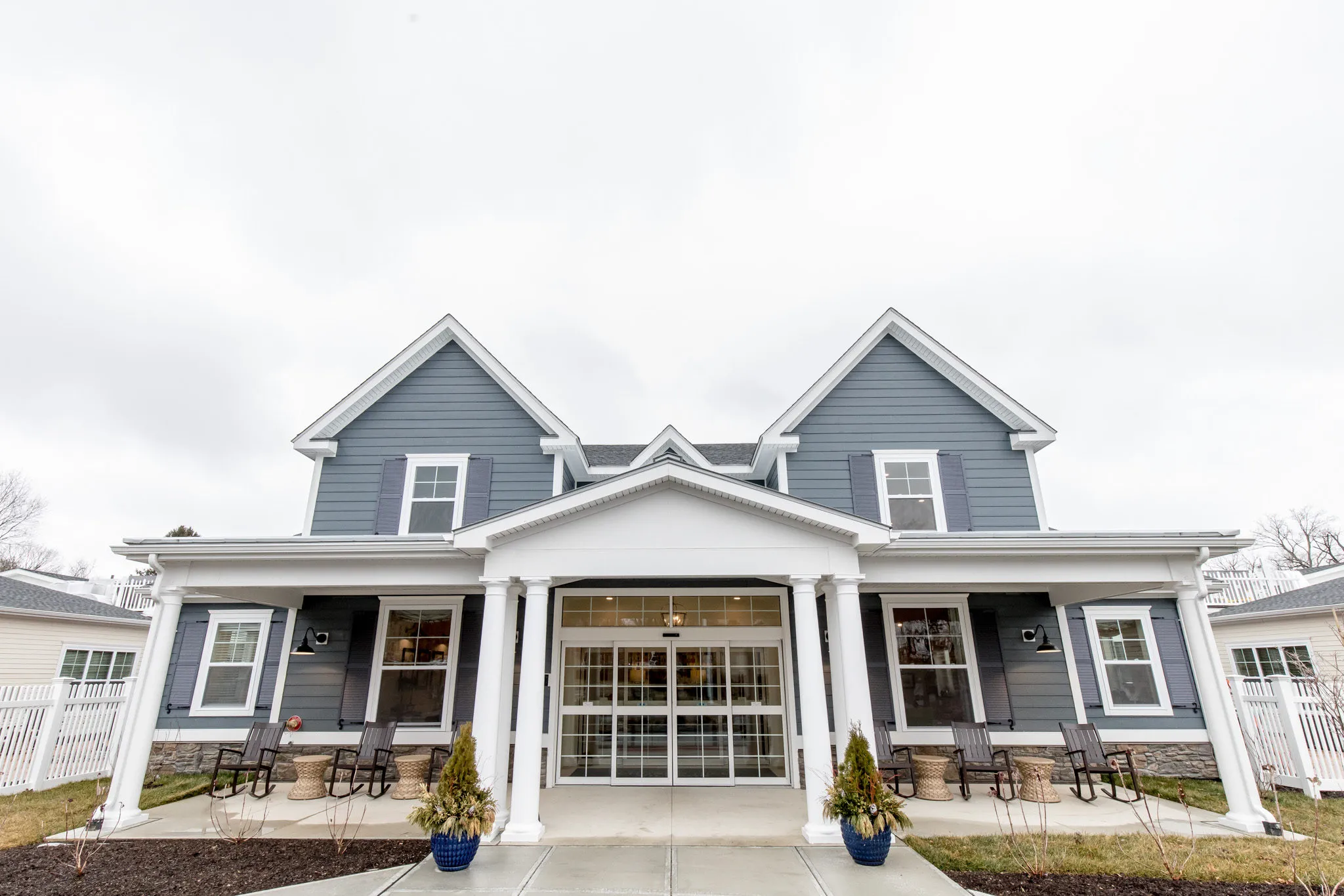 Senior living community exterior with blue clapboard gables above the columned front porch and its rocking chairs