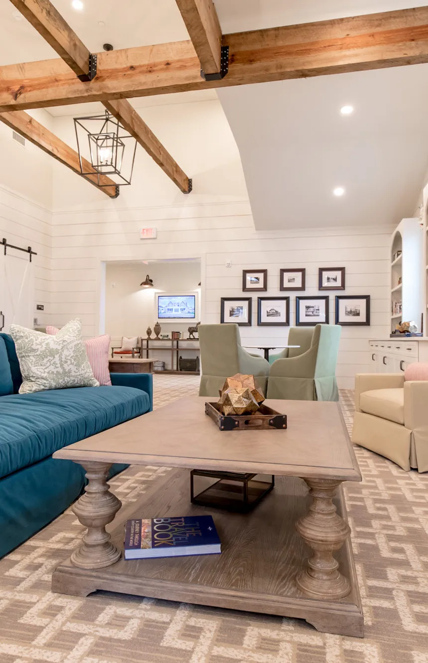 Senior living great room with timber beams and a teal sofa by a linear fireplace, interior design by Banko Design at Church Hill Village, Newtown, Connecticut