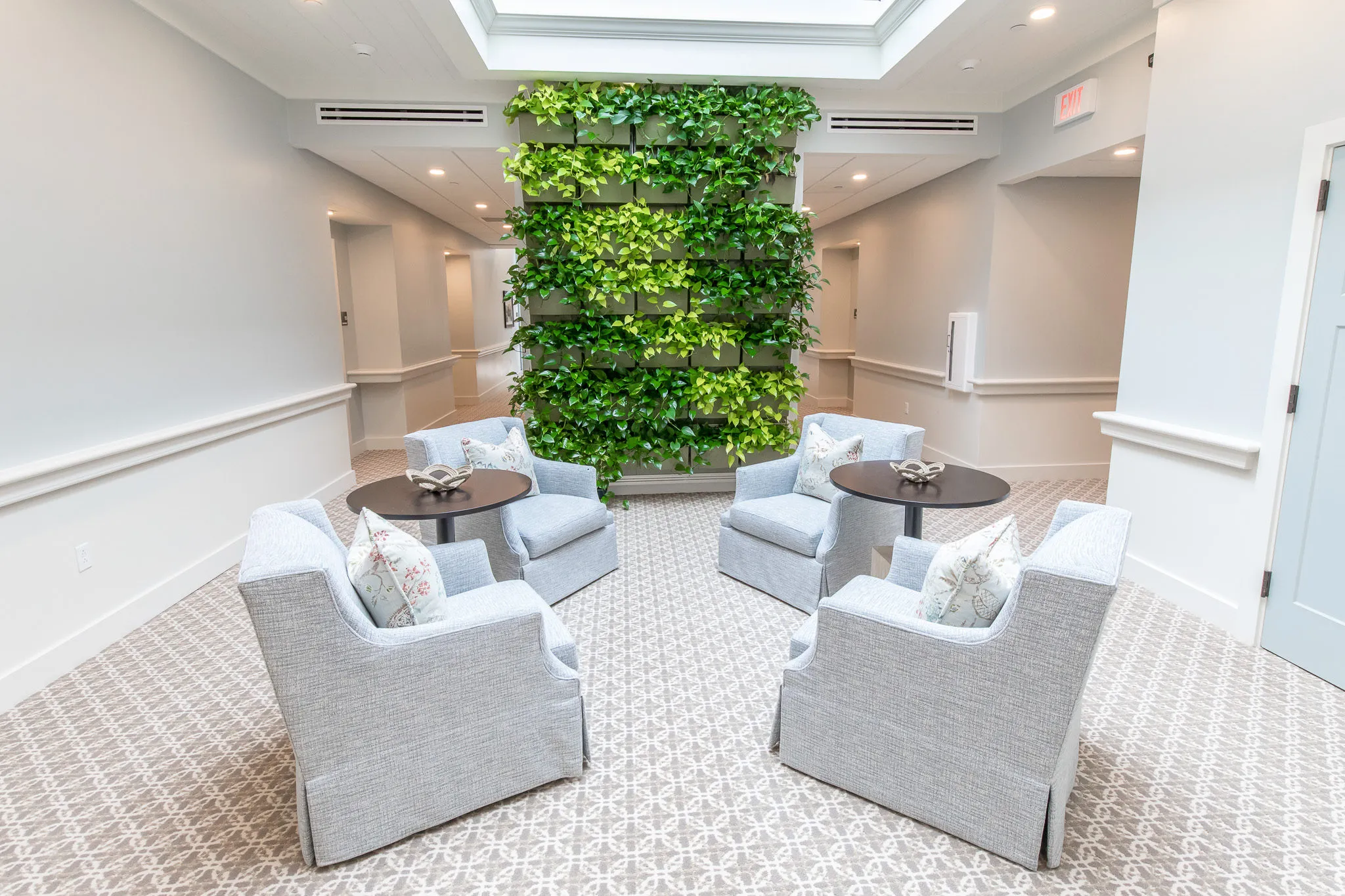 Senior living lounge with a planted living wall between pairs of pale grey armchairs and round side tables