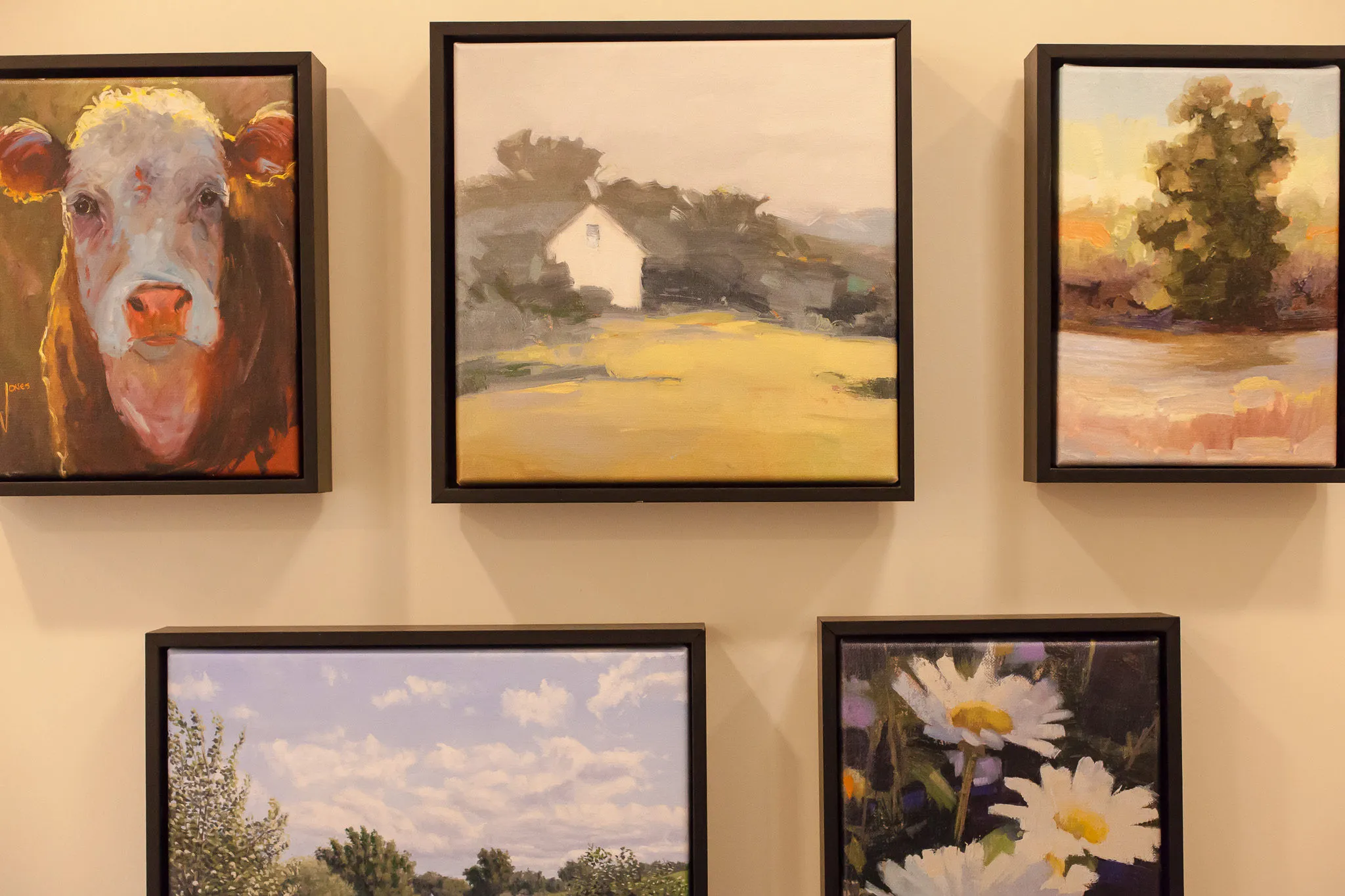 Senior living interior detail: salon-style wall of framed paintings of a cow, a farmhouse, a tree and daisies