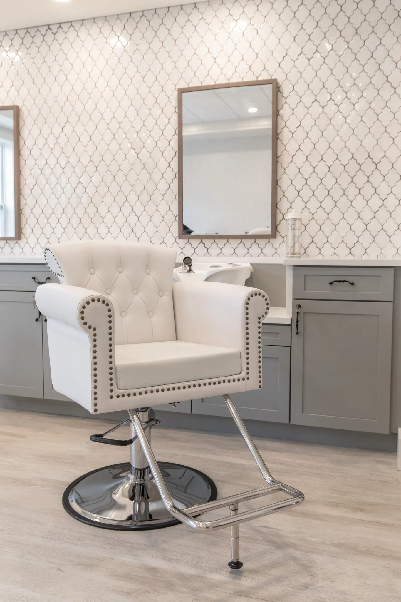 Senior living salon with a tufted white styling chair before grey vanities and mirrors on arabesque tile