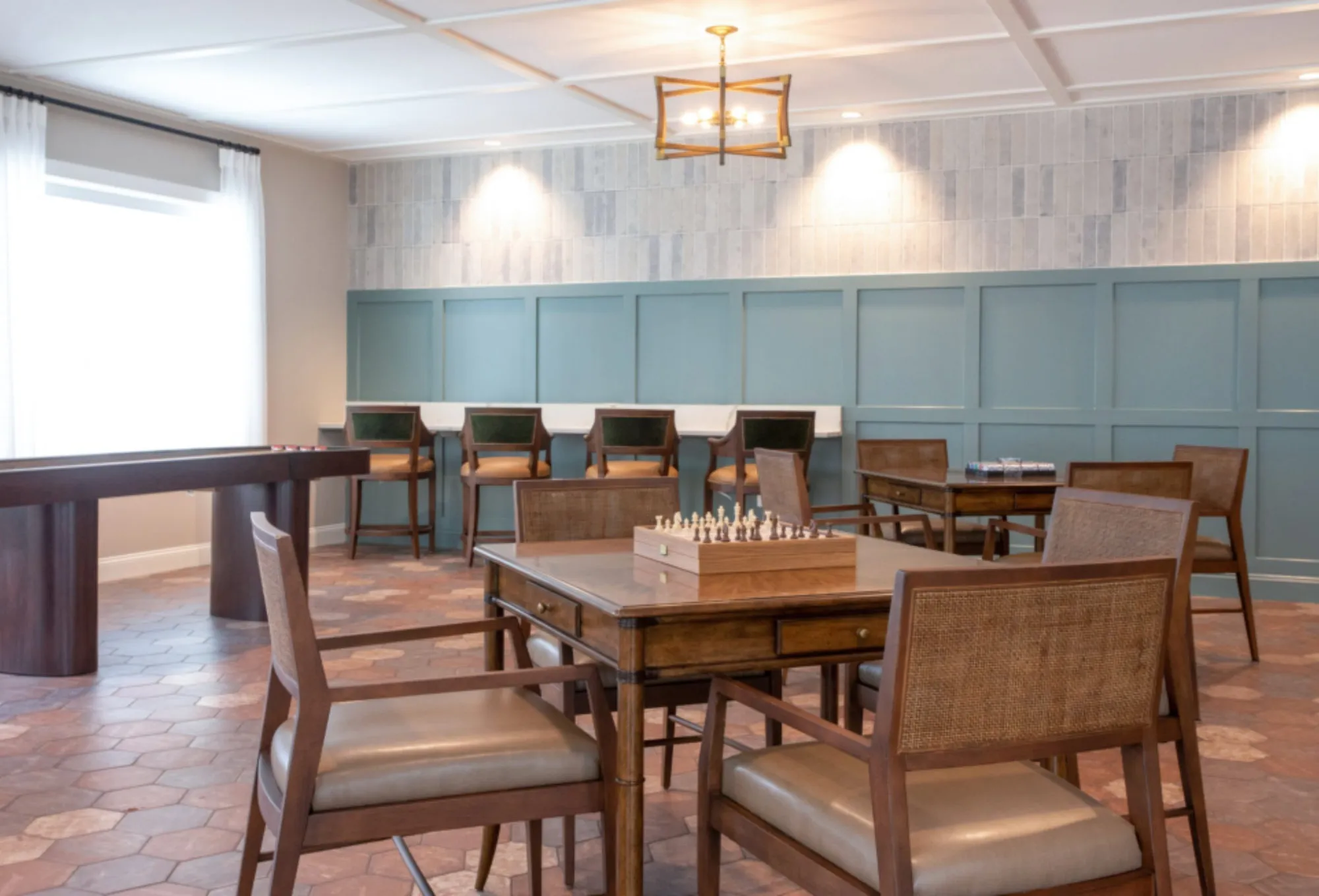 Card room with terracotta hexagon tile, teal panelled walls, inlaid game tables set with chess and a shuffleboard table
