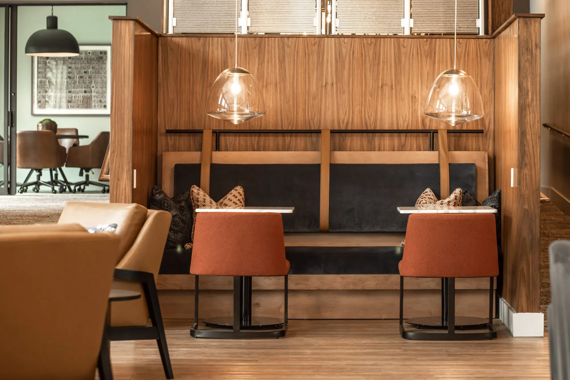 Multifamily amenity walnut booths with navy seat backs and rust chairs at small tables under glass bell pendants