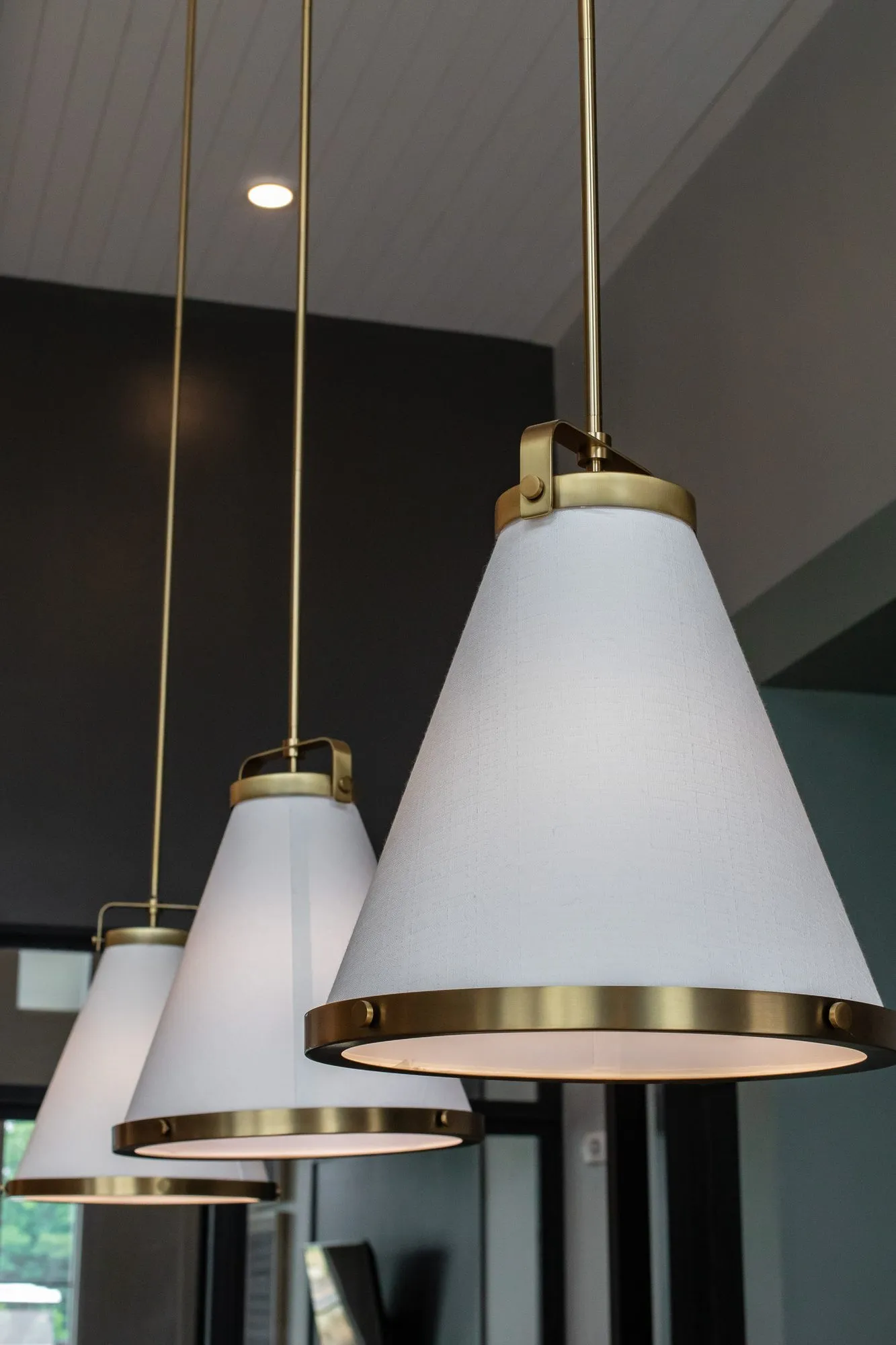Multifamily amenity interior detail: white cone pendants with brass trim hanging against a dark wall