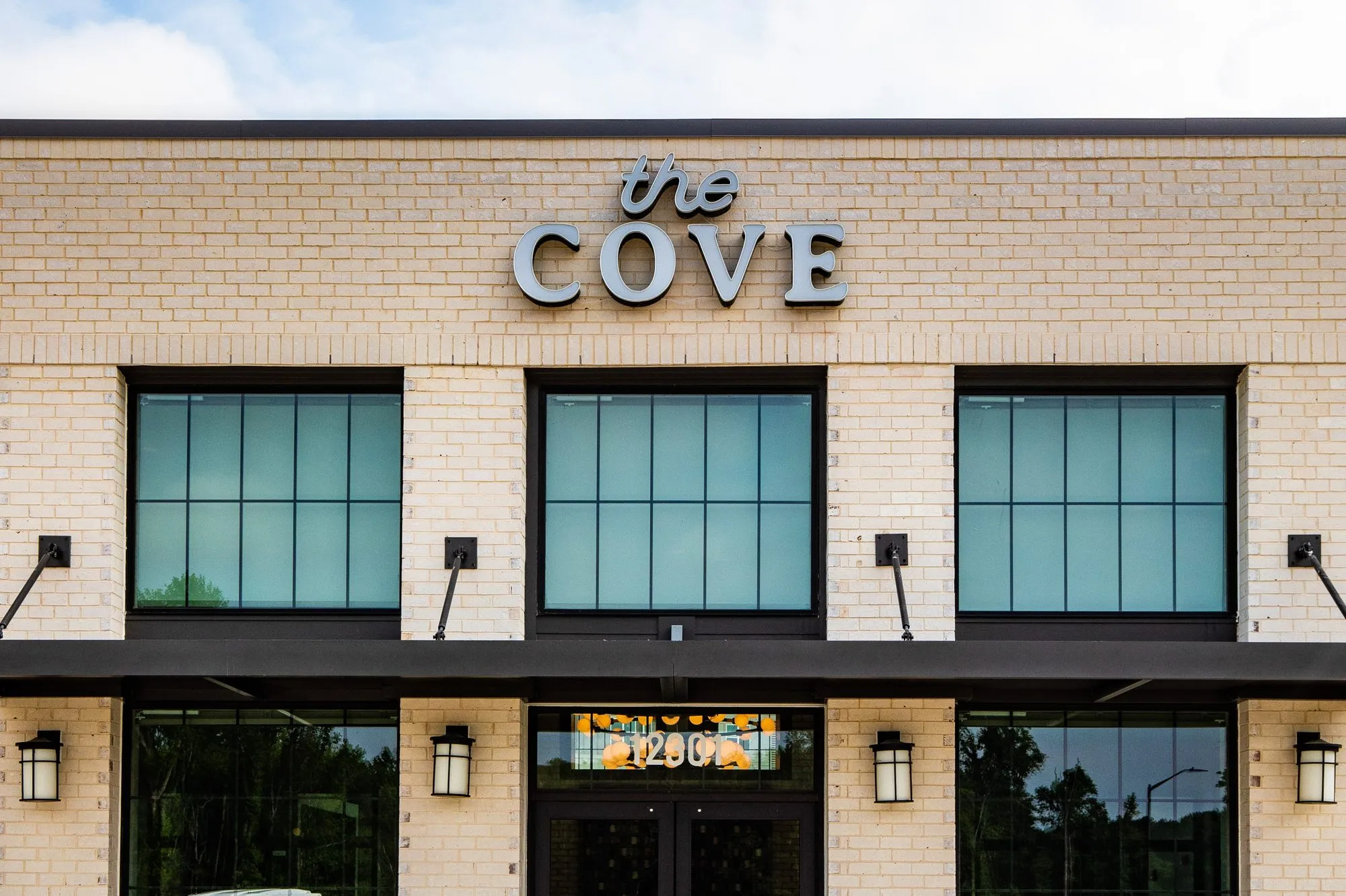 Multifamily community exterior: cream brick facade with black steel windows, lantern sconces and a raised letter sign