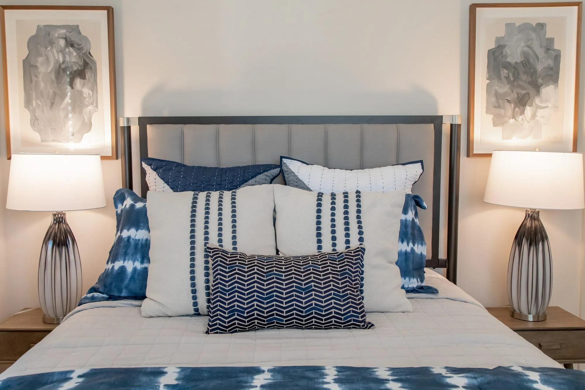 Multifamily apartment bedroom with a grey channel headboard, blue shibori and striped pillows between silver ribbed lamps