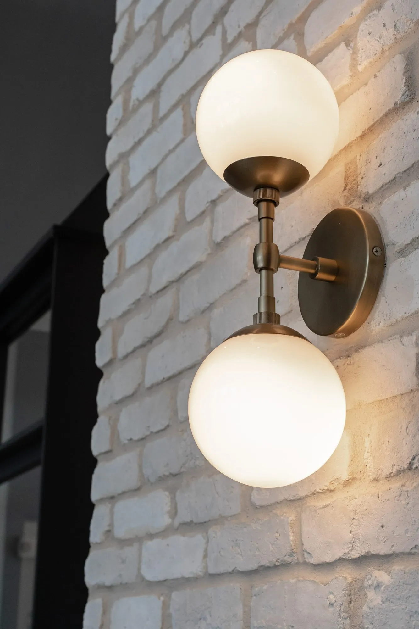 Multifamily amenity interior detail: brass wall sconce with two white glass globes on whitewashed brick