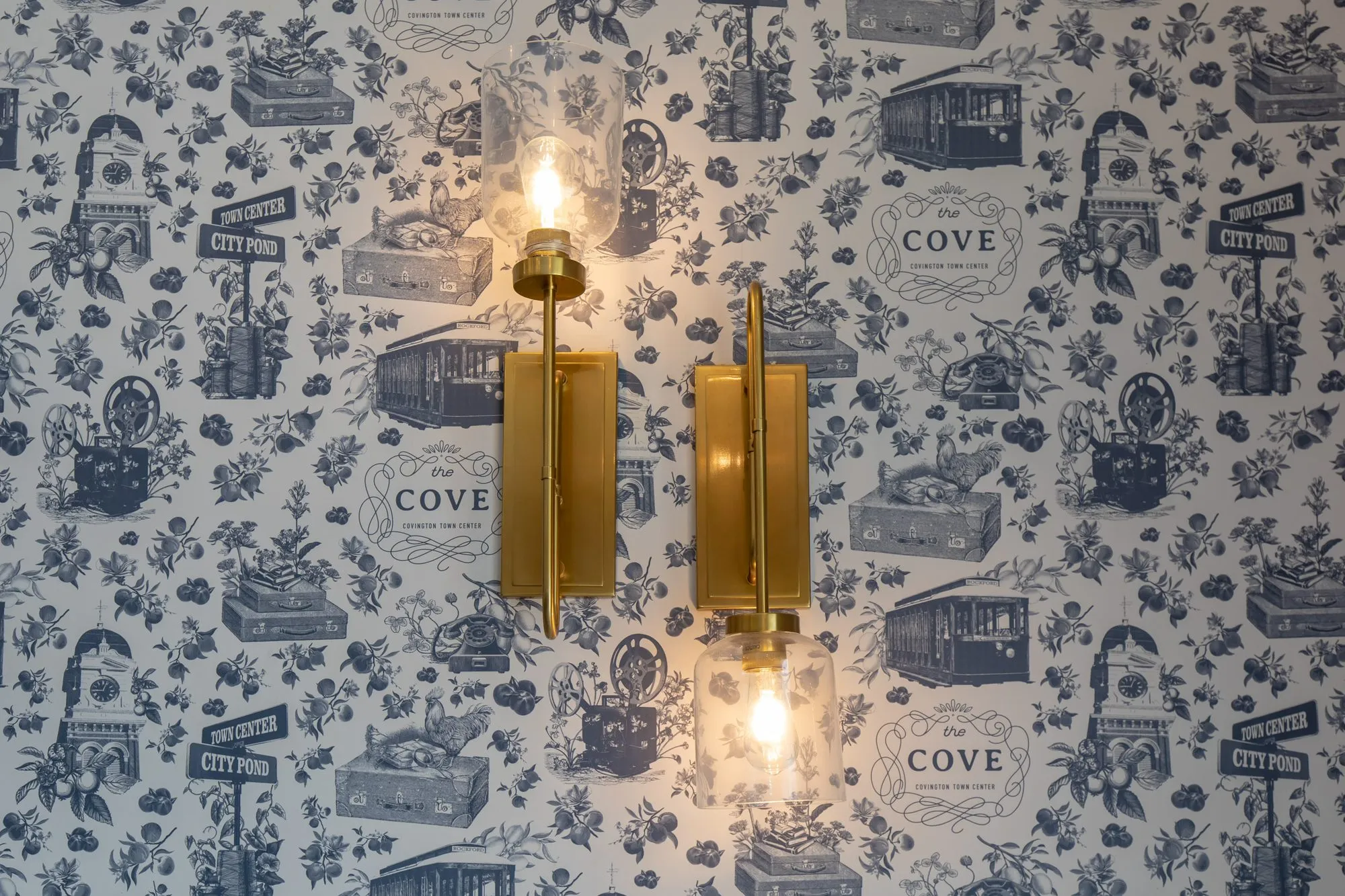 Multifamily amenity game room sconces with clear glass shades on navy and white toile wallpaper of trolleys and town scenes