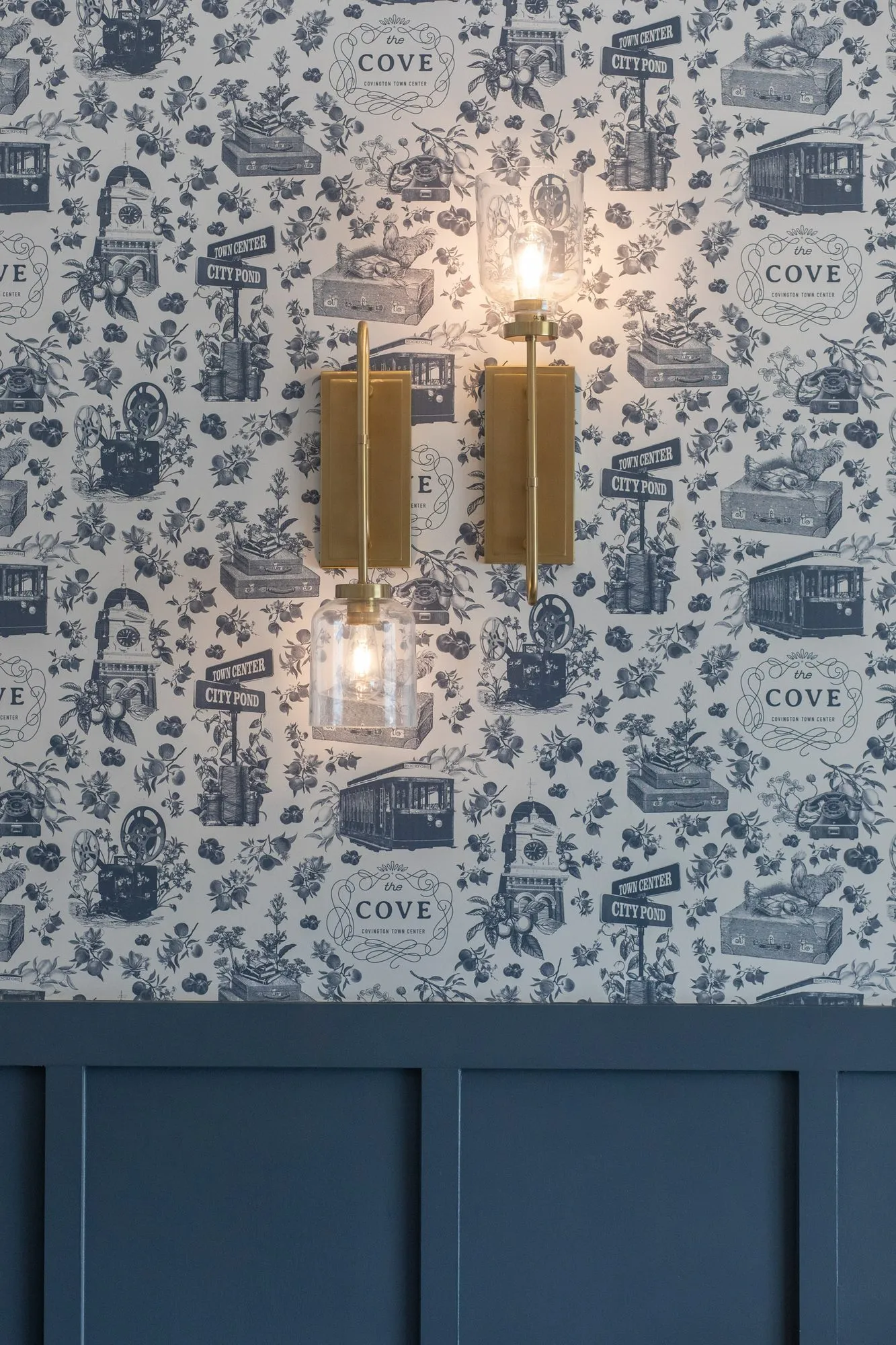 Multifamily amenity game room wall, a brass sconce on navy and white toile wallpaper above navy wainscot