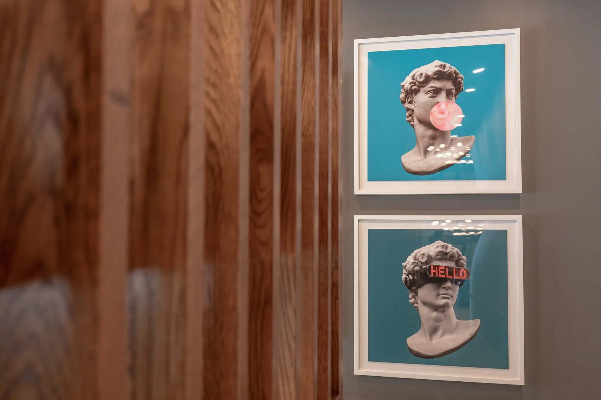 Multifamily amenity art wall: two framed pop art prints of a classical bust on teal, one blowing pink bubble gum