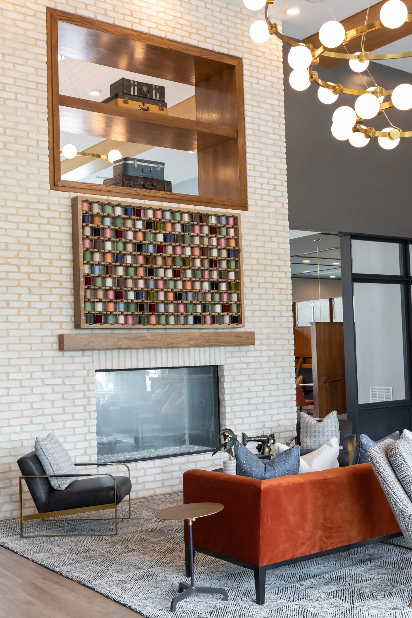 Multifamily amenity lounge fireplace wall with a wood niche and framed spool grid above a black armchair and rust sofa