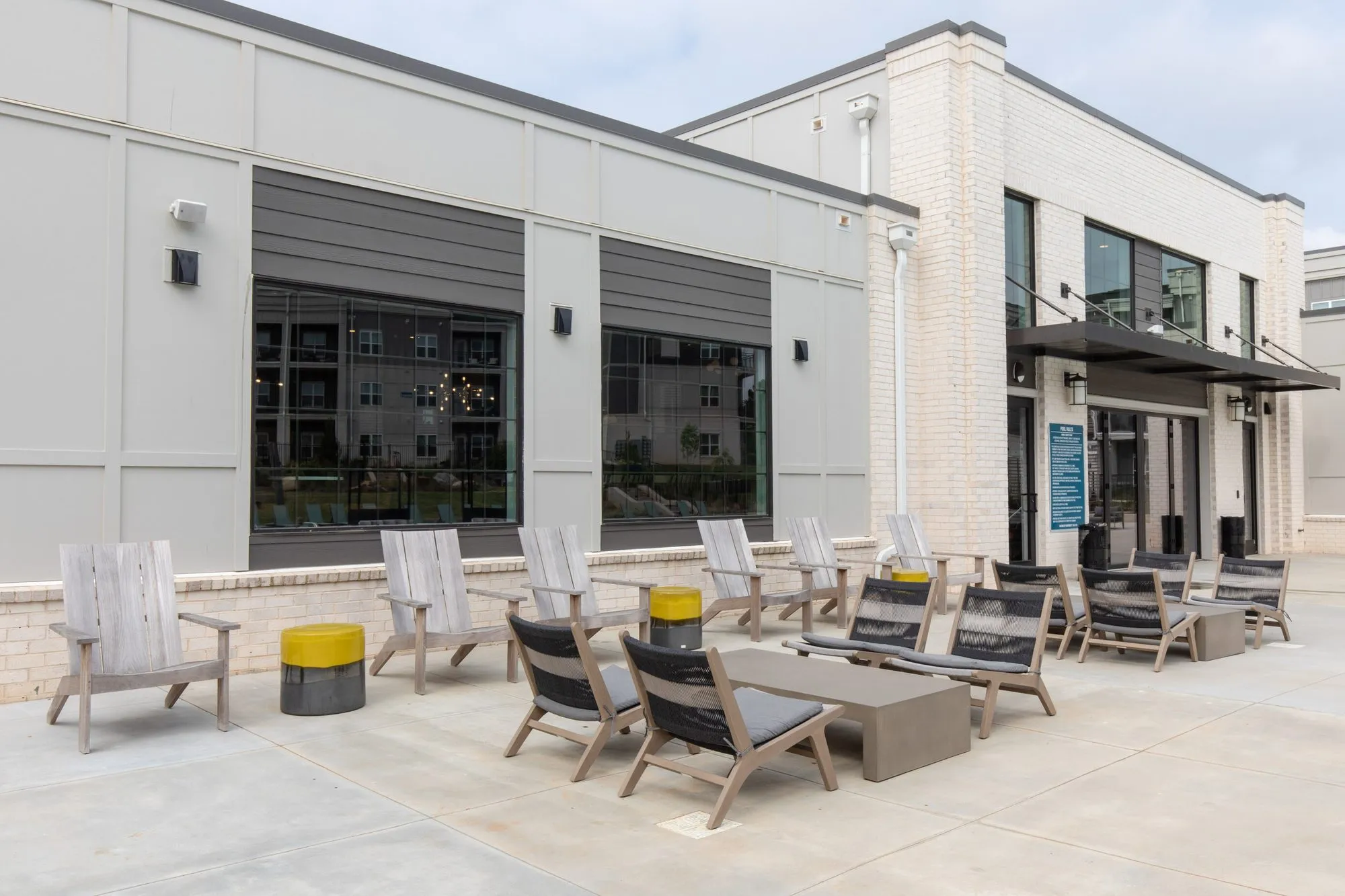 Multifamily community patio with grey Adirondack chairs and black sling chairs around low tables beside the brick clubhouse