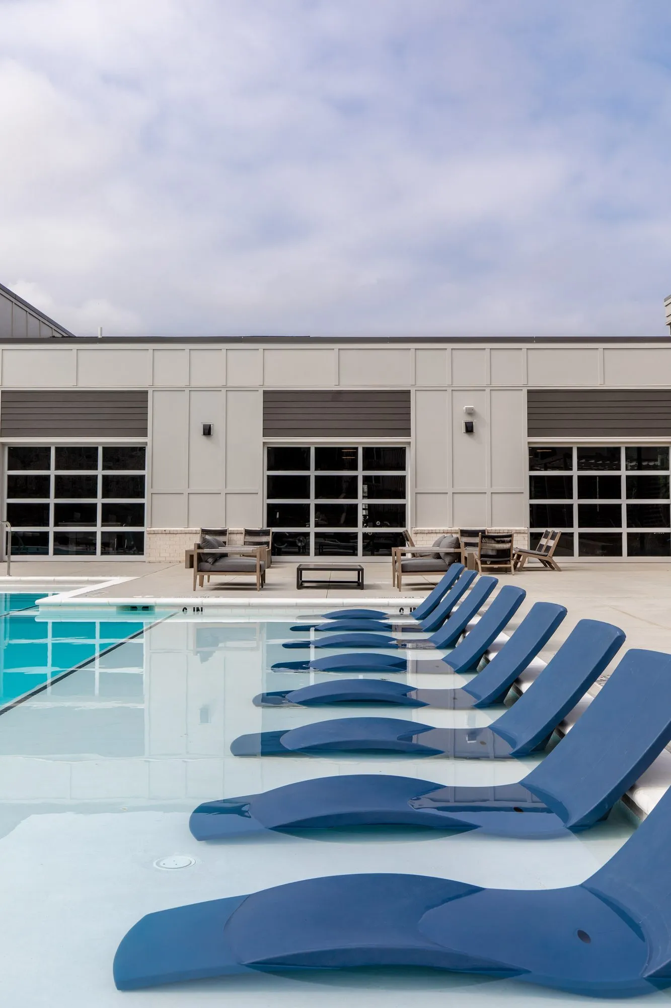 Multifamily community pool with navy loungers on the shallow sun shelf, the clubhouse with glass garage doors beyond