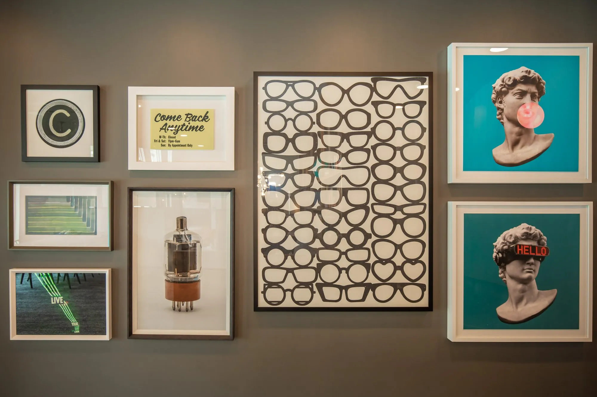 Multifamily amenity art wall of framed prints on grey, among them a grid of eyeglasses, a vacuum tube and pop art busts