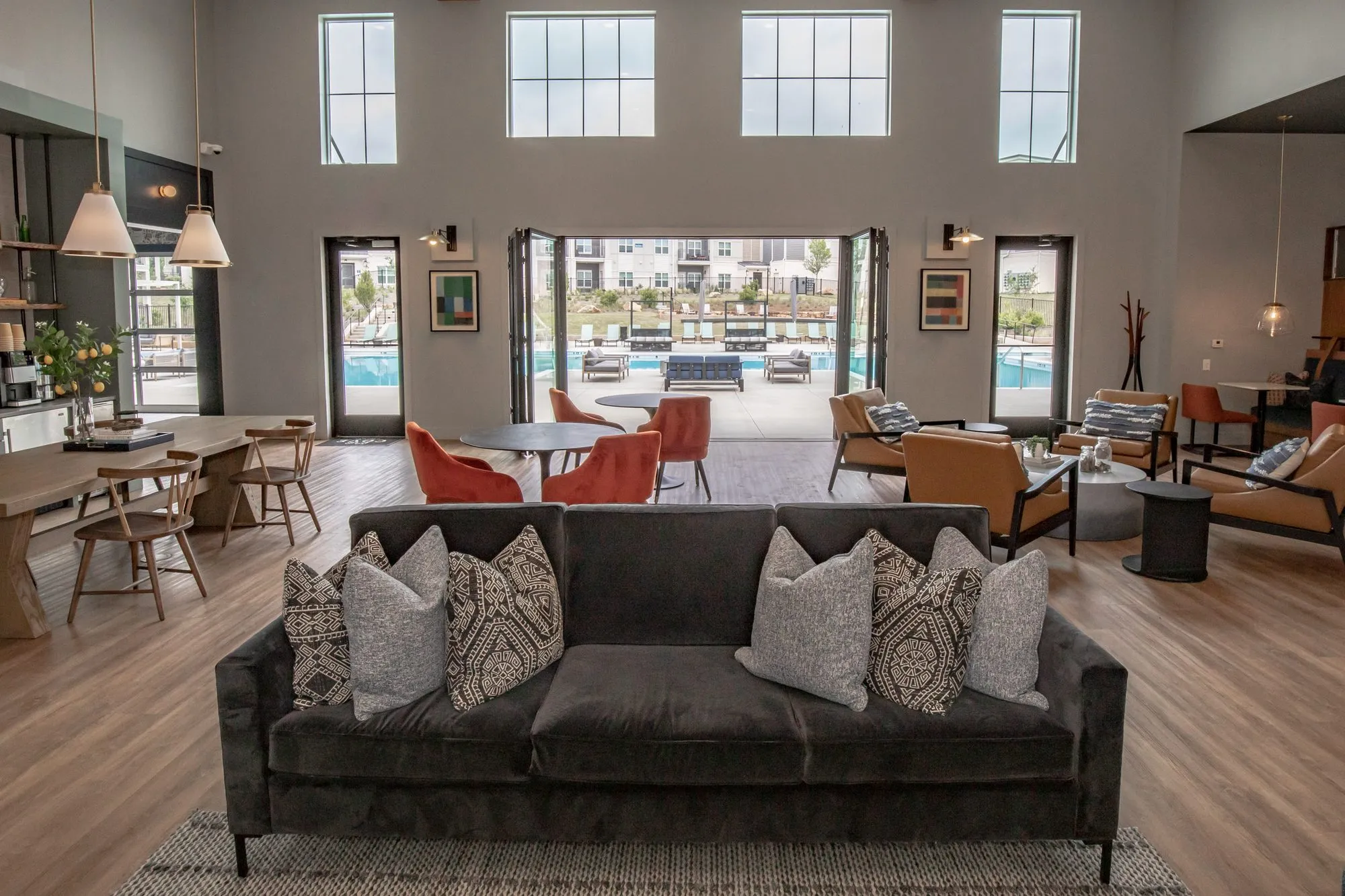 Multifamily amenity clubhouse seen past a dark velvet sofa, orange chairs at tables and open glass doors to the pool