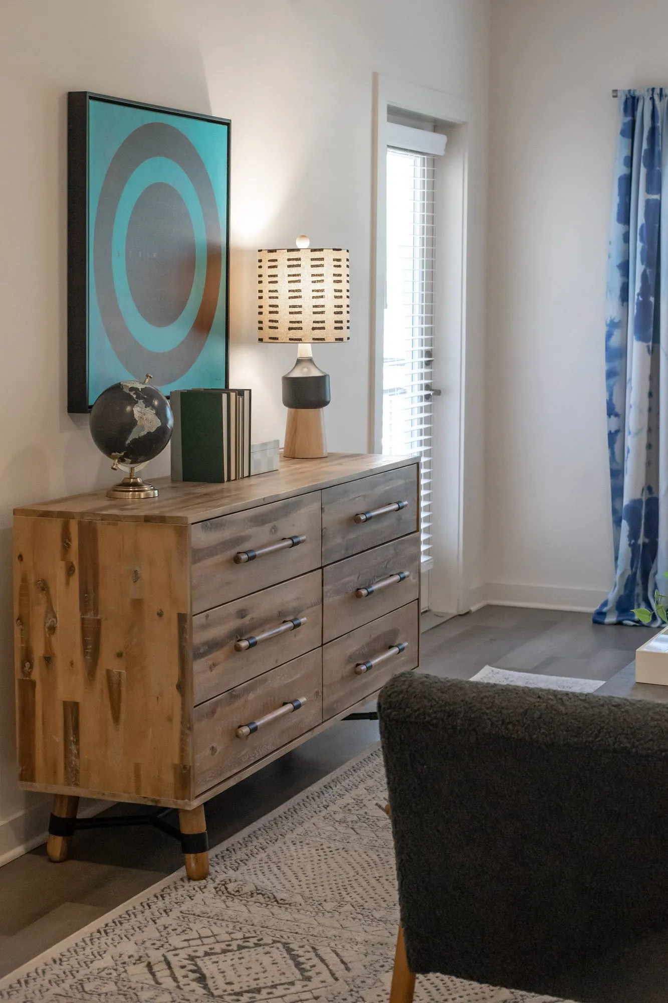 Multifamily apartment model living room with a reclaimed wood dresser, a globe and a teal concentric circle artwork