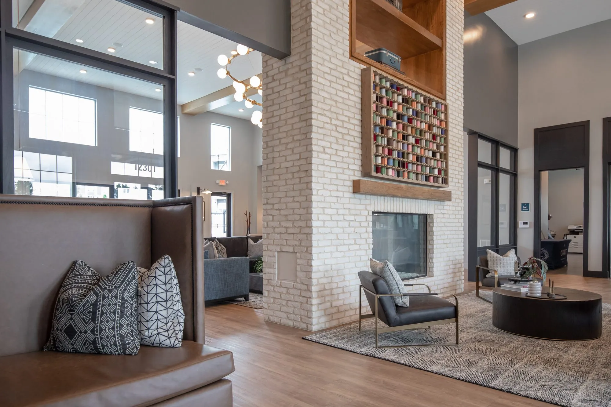 Multifamily amenity lounge seen from a tan leather booth with patterned pillows to the white brick fireplace and spools