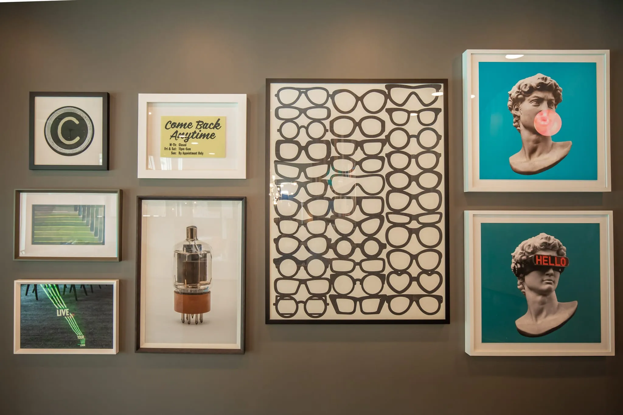Multifamily amenity art wall of framed prints and two teal bubblegum busts around a print of rows of eyeglass frames