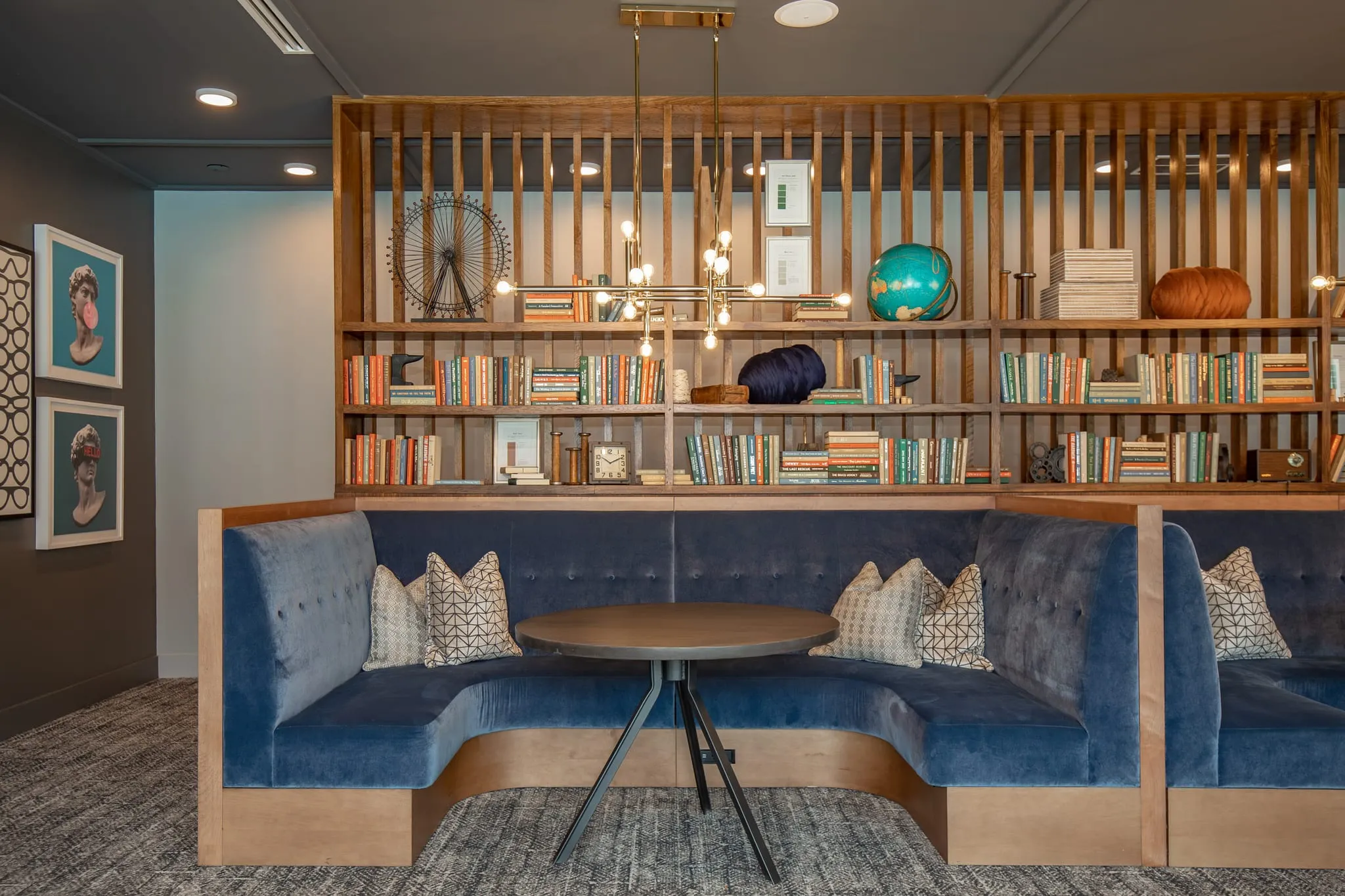 Multifamily amenity booth nook with a curved navy banquette and round table framed by a wood slat and bookshelf screen