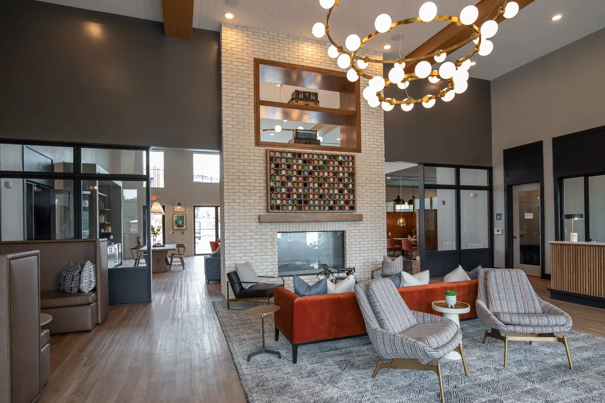 Multifamily amenity double height lounge with a whitewashed brick fireplace, a framed thread spool grid and a rust sofa
