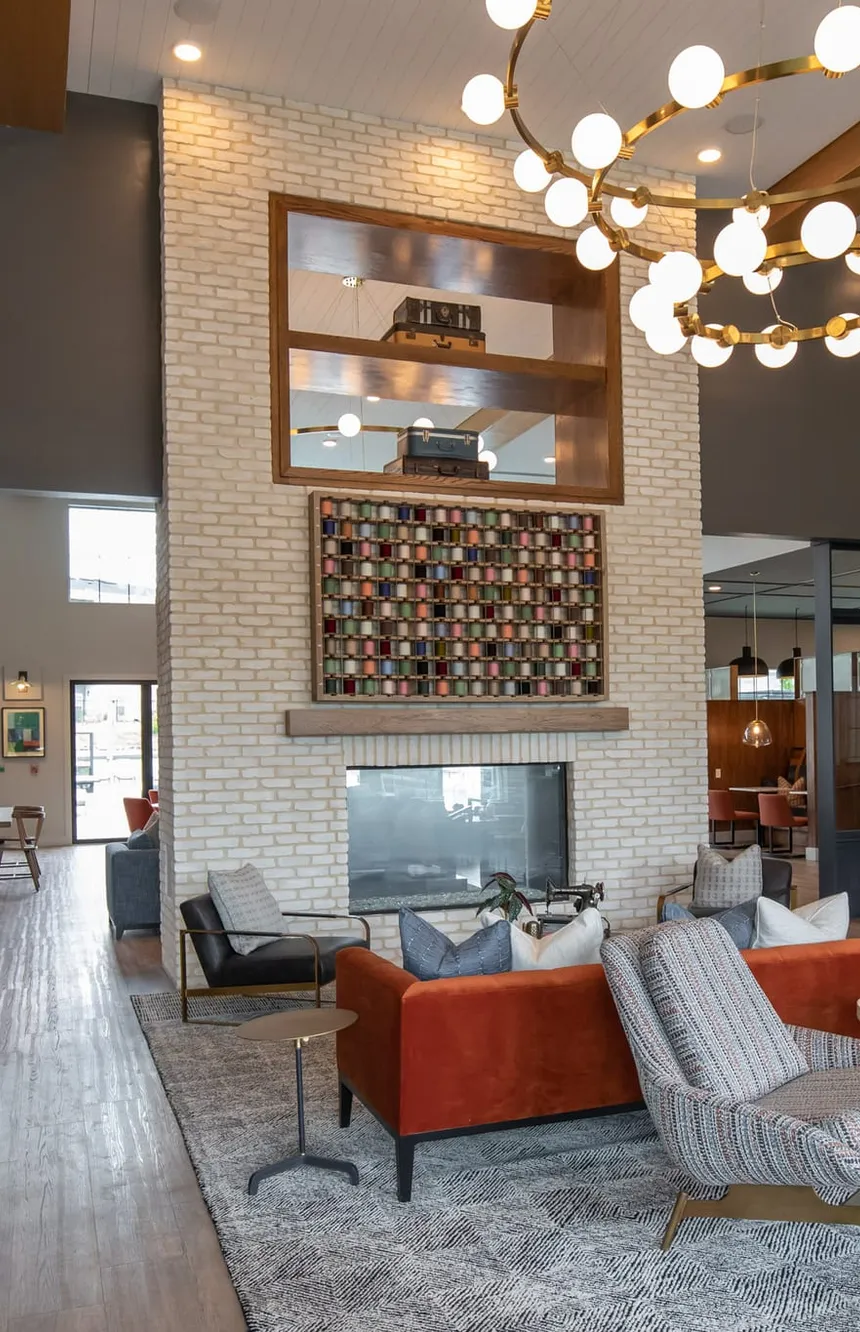 Multifamily amenity double height lounge with a white brick fireplace and rust sofa, interior design by Banko Design at Cove at Covington, Covington, Georgia