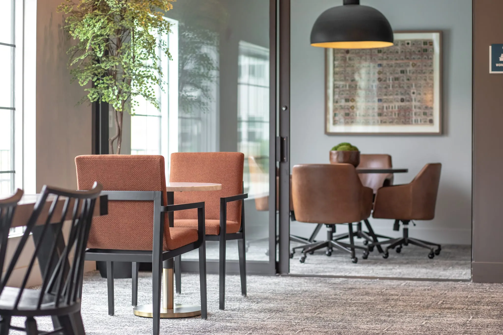 Multifamily amenity conference room with orange armchairs in the foreground and a meeting table beyond the glass wall