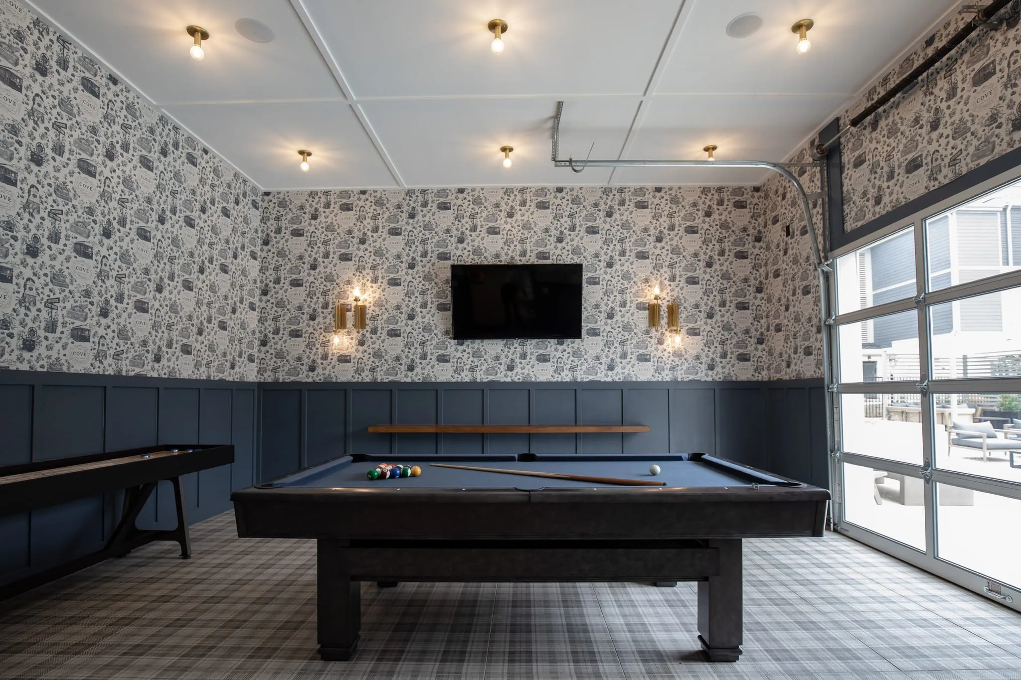 Multifamily amenity game room with a billiards table and shuffleboard below toile wallcovering and navy wainscot