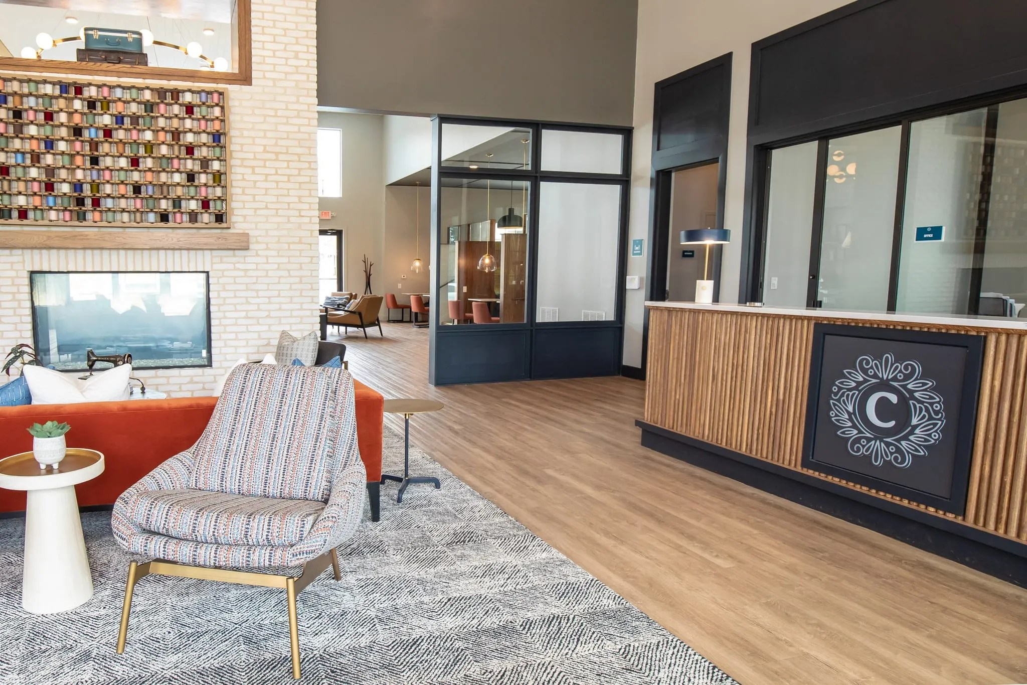 Multifamily amenity leasing lounge, a framed spool display over a fireplace on white brick, an orange sofa and leasing desk