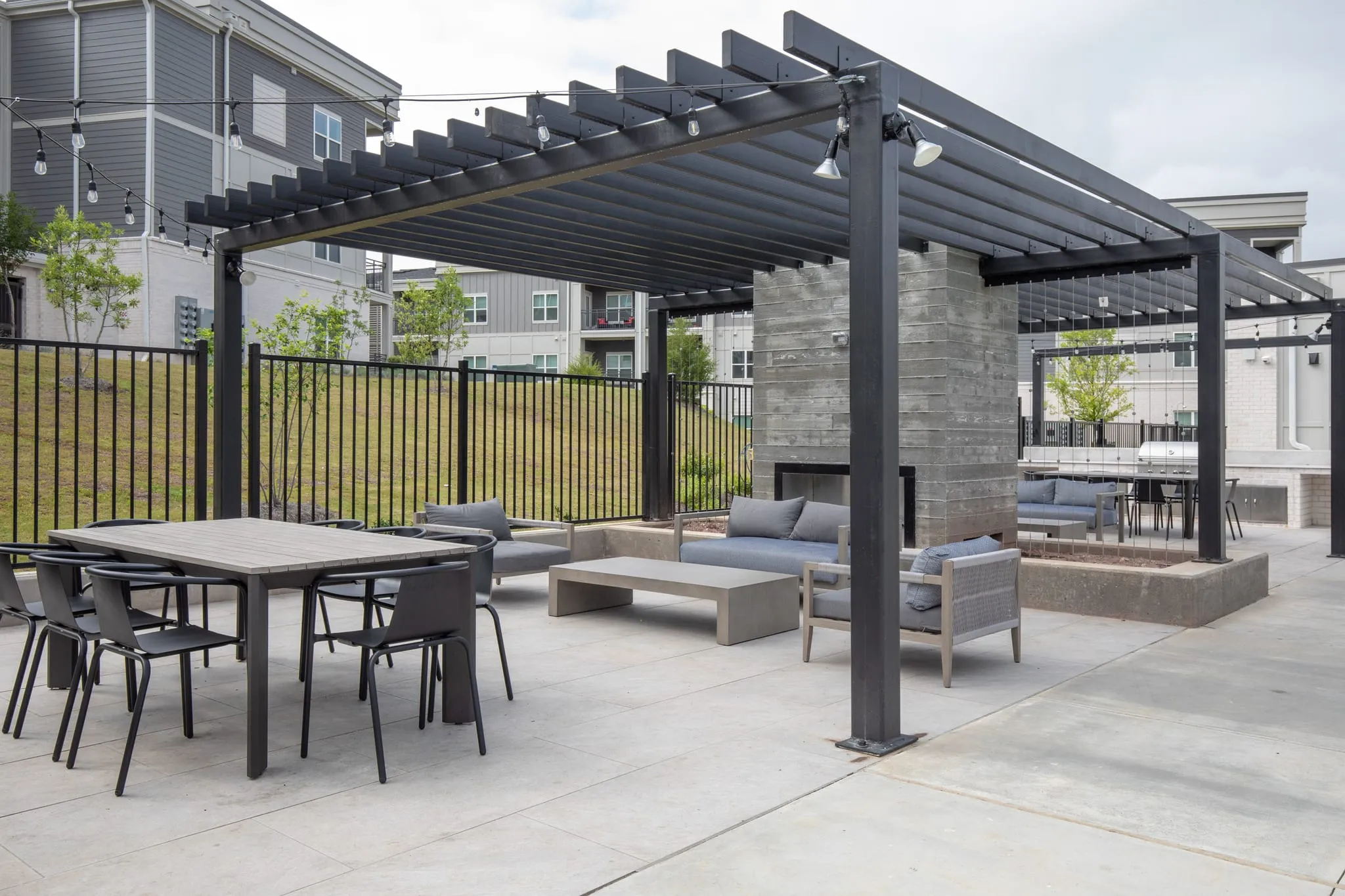 Multifamily community courtyard with dining tables and lounge sofas under the pergola beside the outdoor fireplace